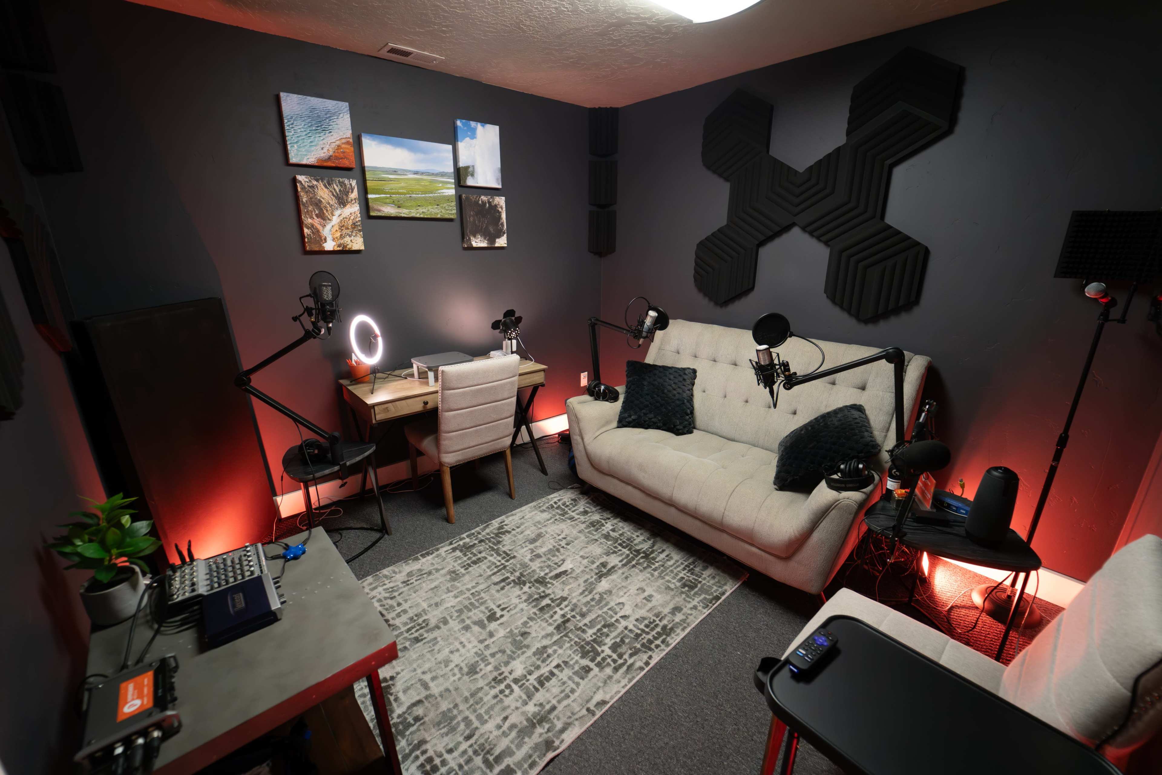 A modern recording studio features a sofa, desk with microphones, and wall-mounted acoustic panels, illuminated by soft lighting.