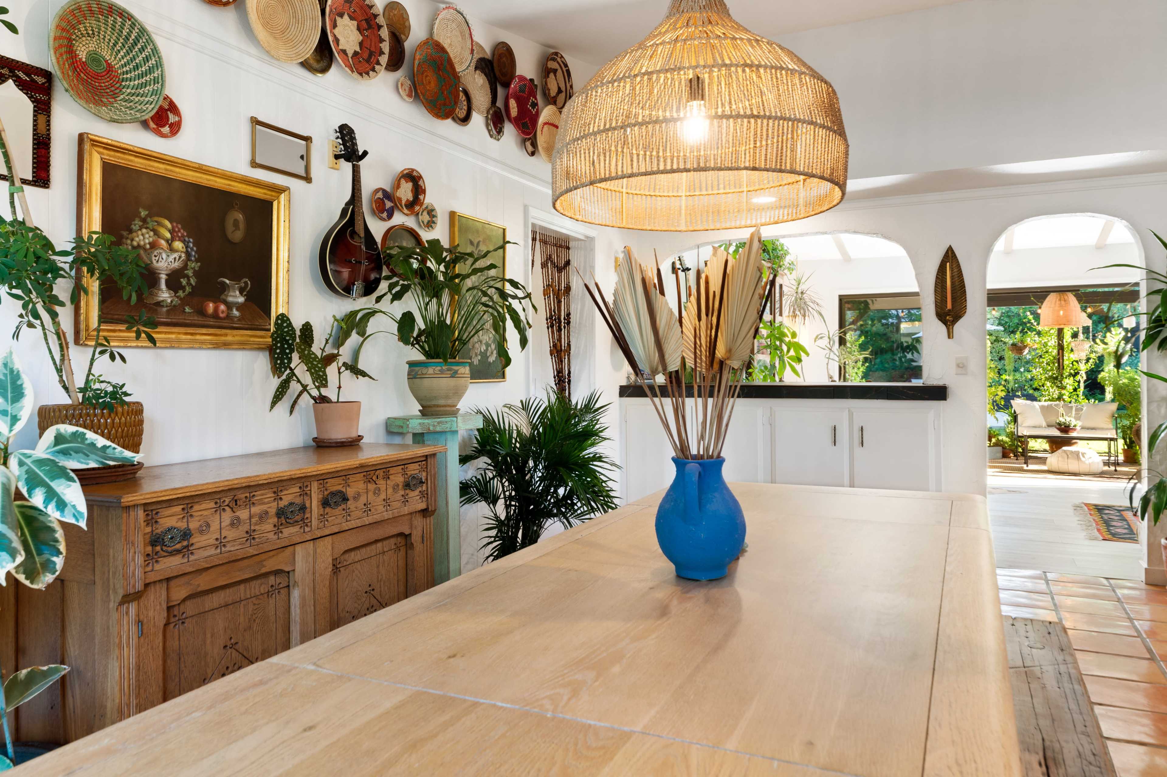A dining area with a wooden table, a blue vase filled with decorative plants, and various decorative items and artworks on the walls.