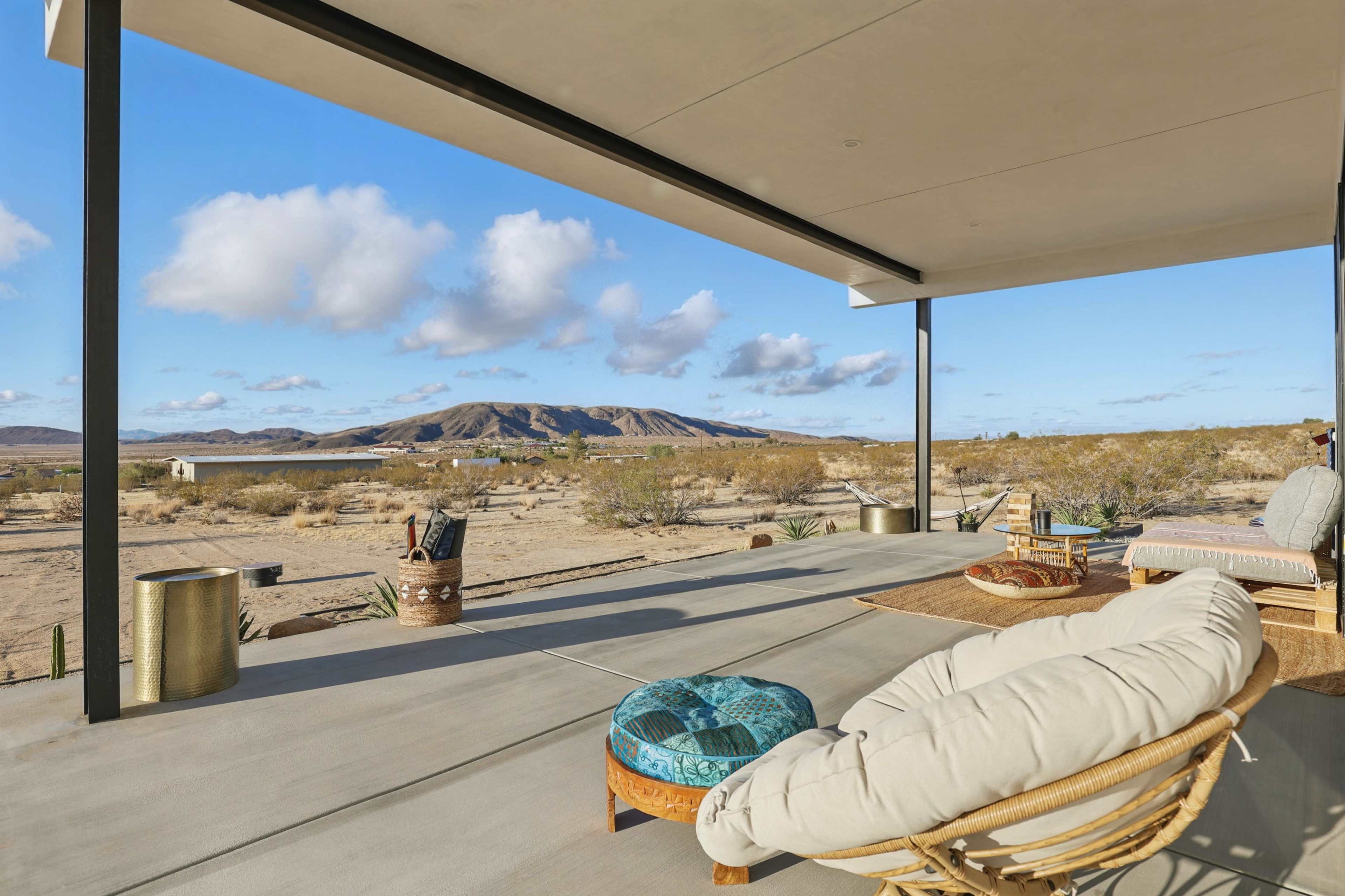 A covered patio overlooks a desert landscape with mountains in the background and sparse vegetation.