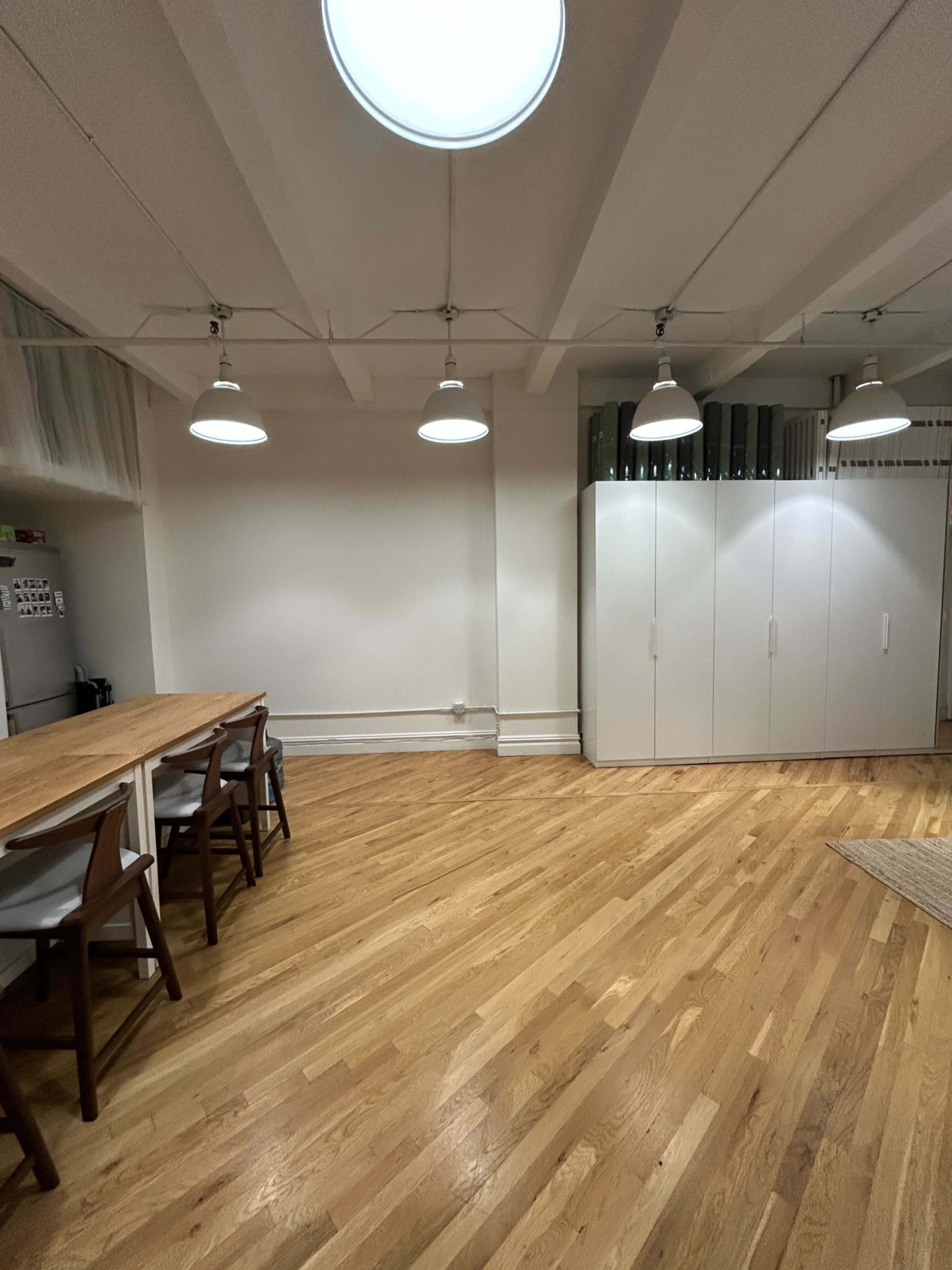 A spacious, well-lit room features a wooden table with chairs, and a cabinetry wall, all set on a polished wooden floor.