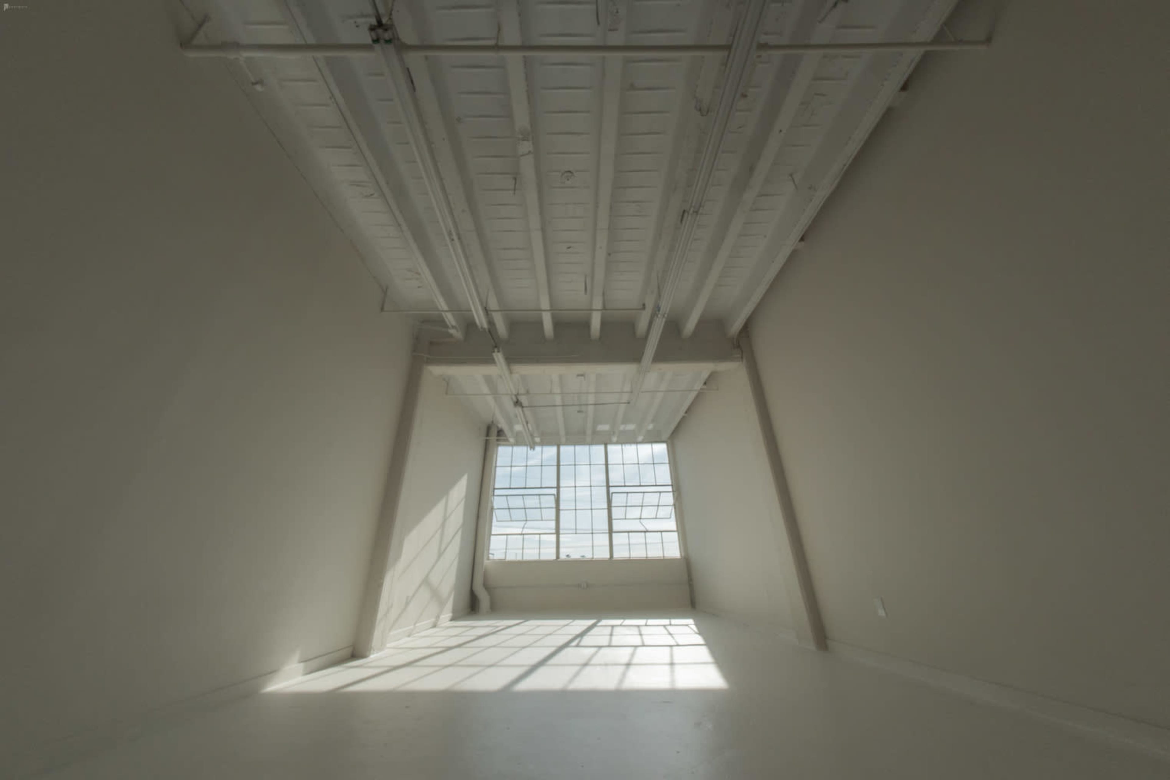 A spacious, empty room features large windows that allow natural light to stream in, highlighting the angular walls and ceiling.