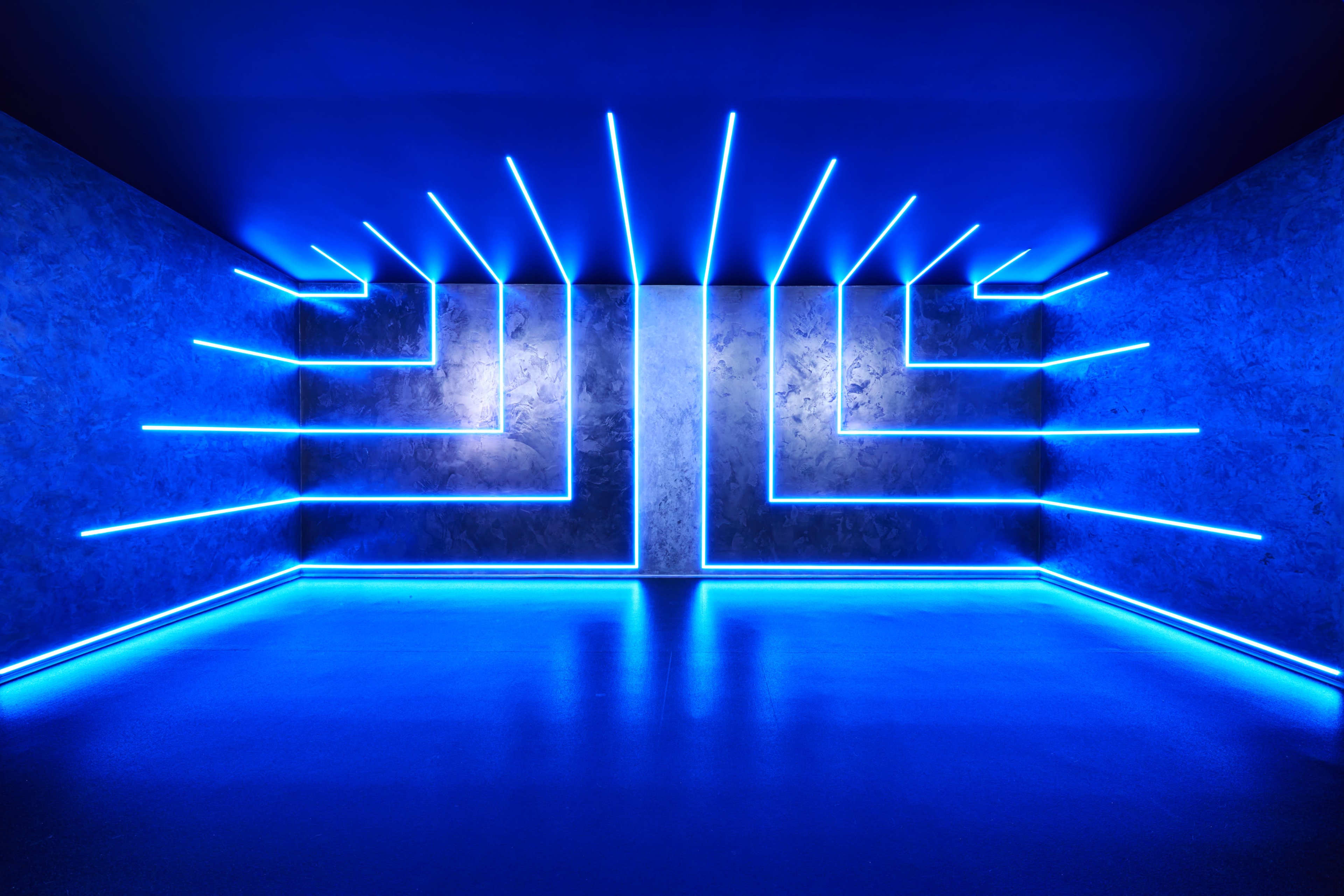 The image features a minimalist interior space with blue neon light strips arranged geometrically on the walls and floor.