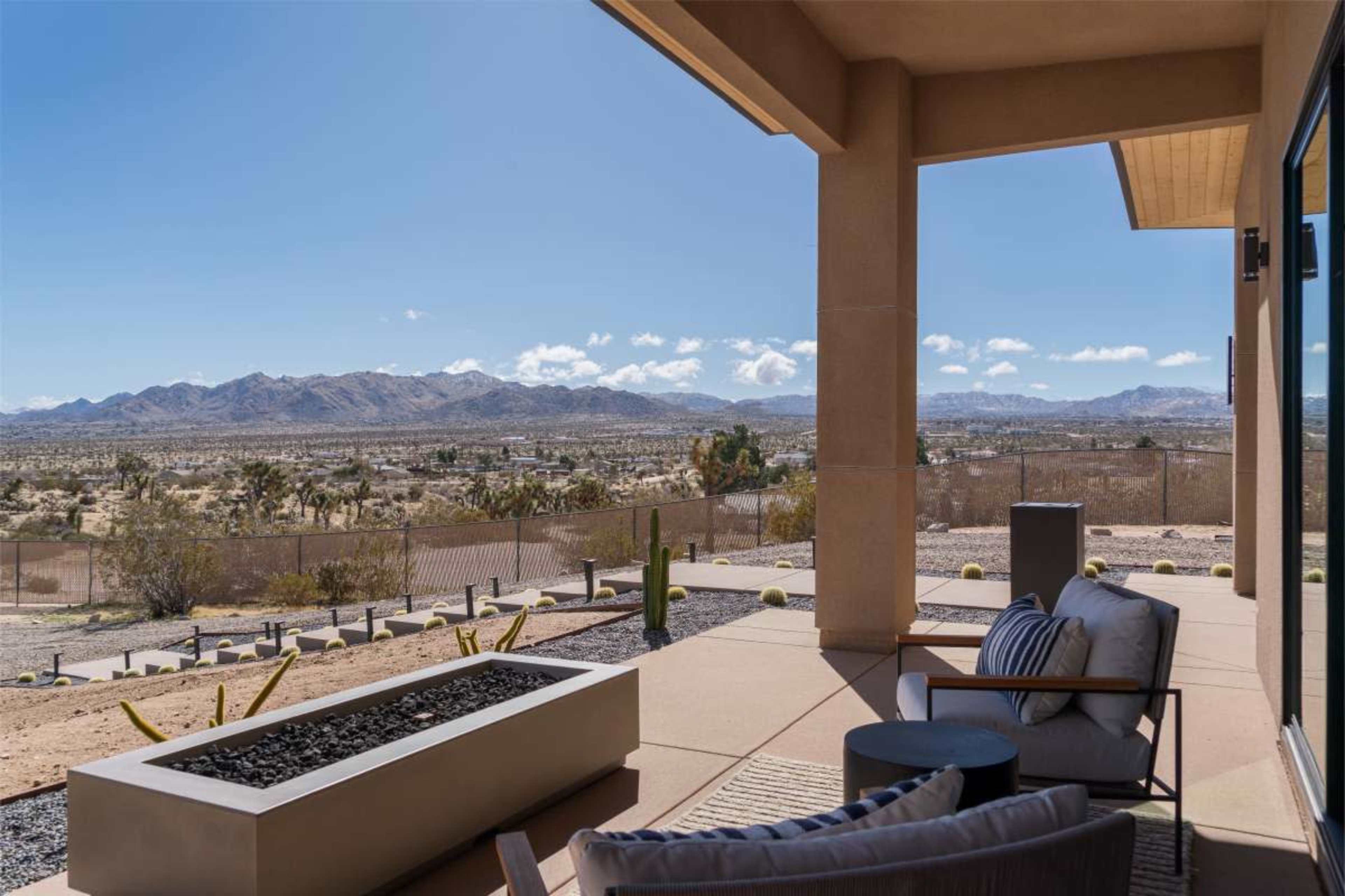 A patio with modern furniture overlooks a desert landscape with mountains in the distance under a clear blue sky.