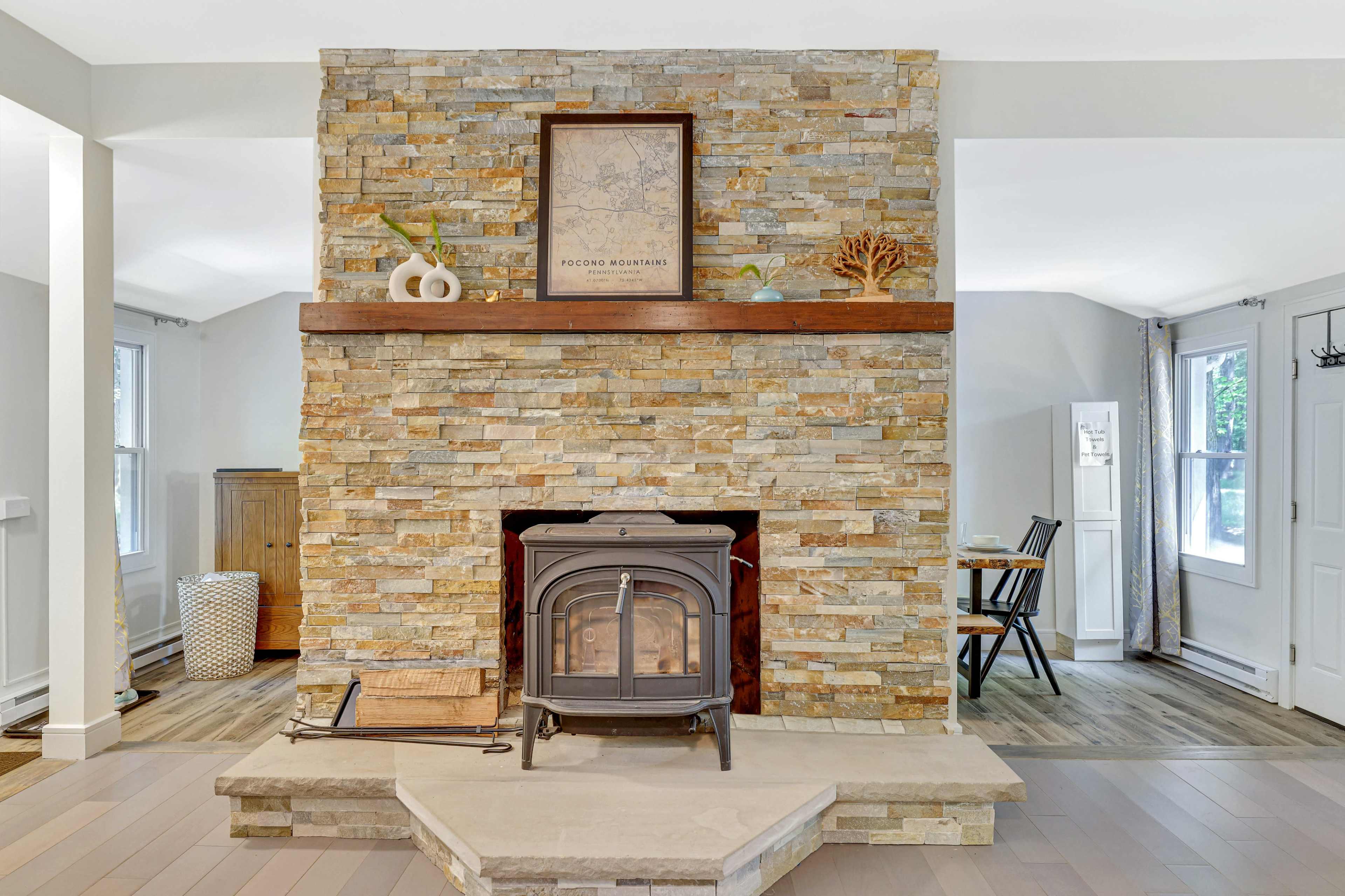A living room featuring a stone fireplace with a woodstove, framed artwork above it, and a dining area visible in the background.