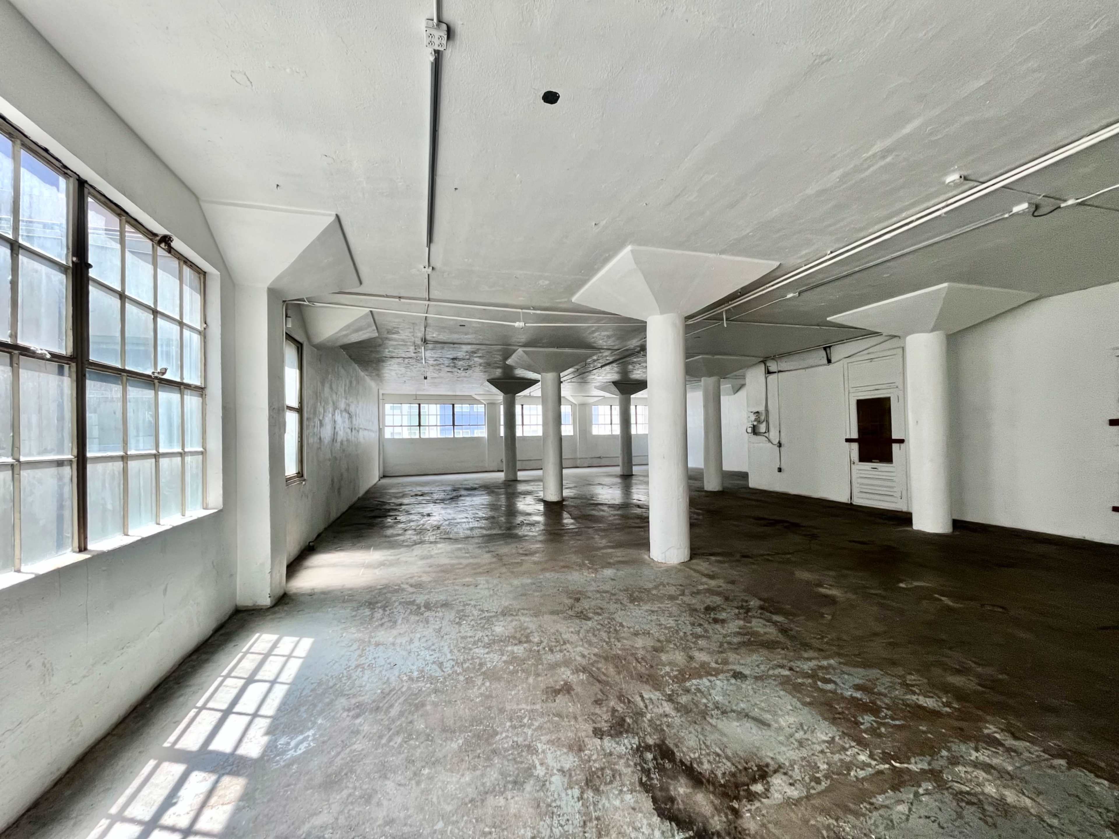 A large, empty room with concrete flooring and several windows allowing light to enter.