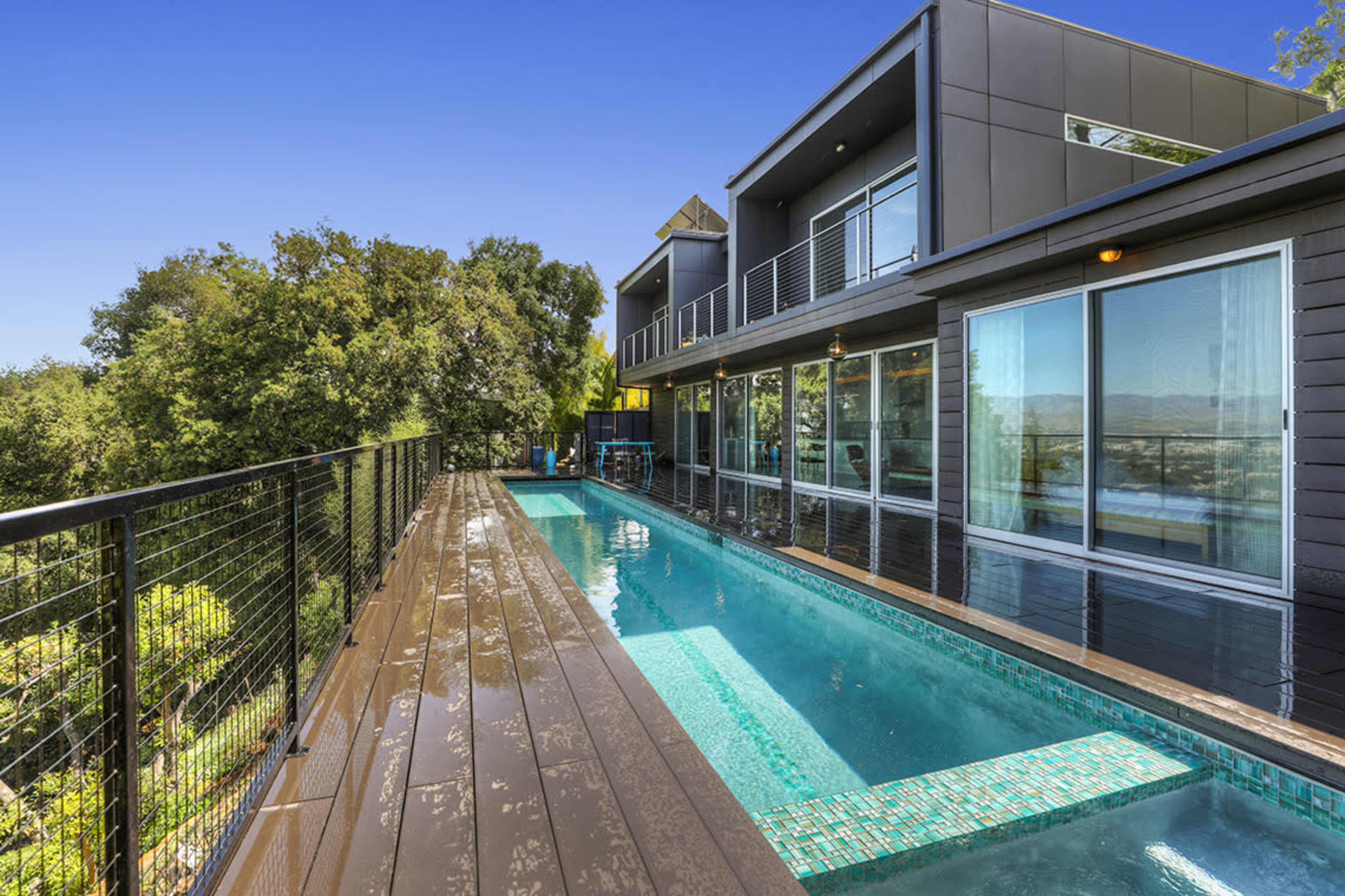 A modern house with large windows and a wooden deck alongside a swimming pool.