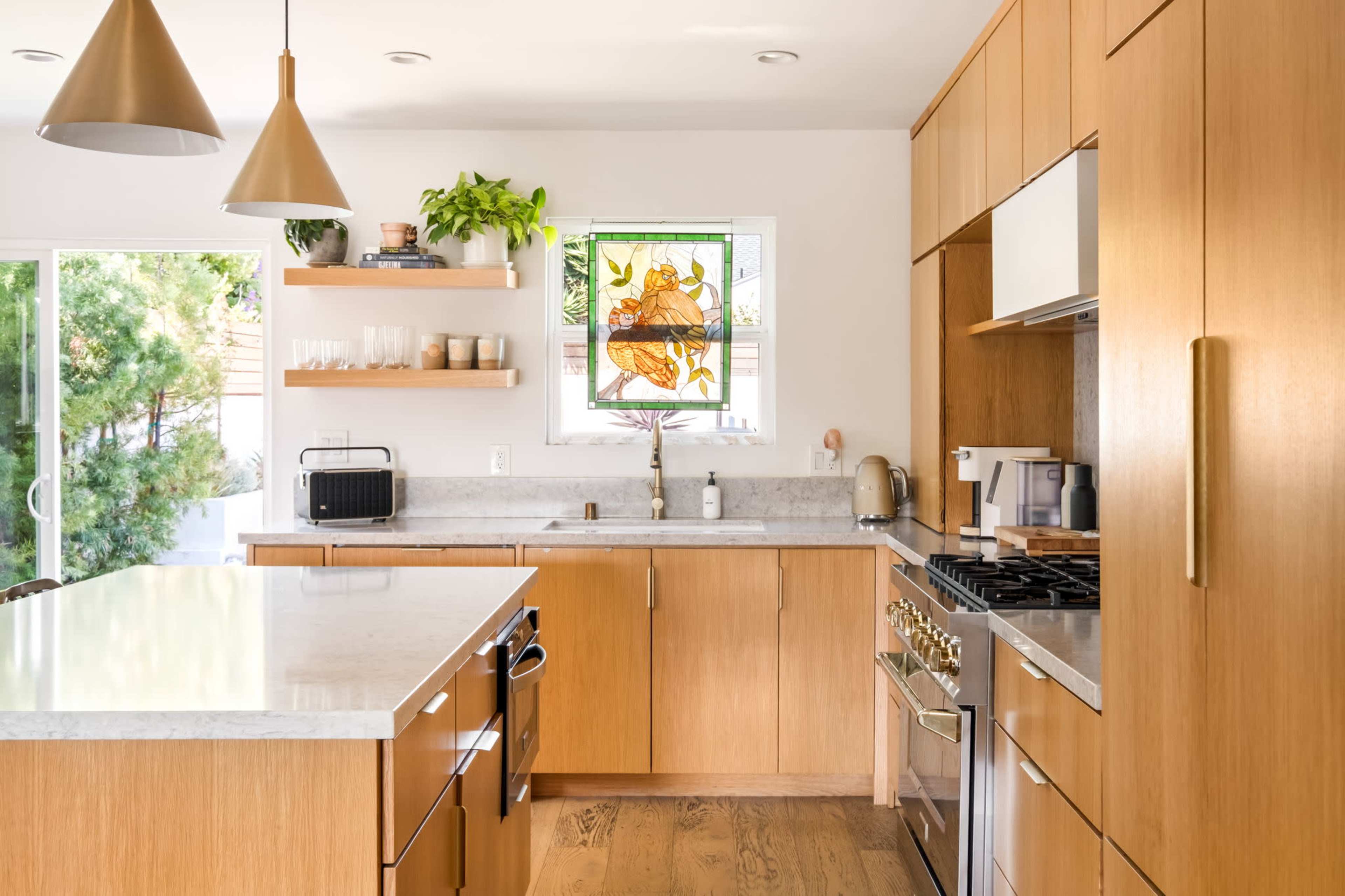 The image shows a modern kitchen with wooden cabinetry, a large island, and a stained glass window featuring a decorative design.