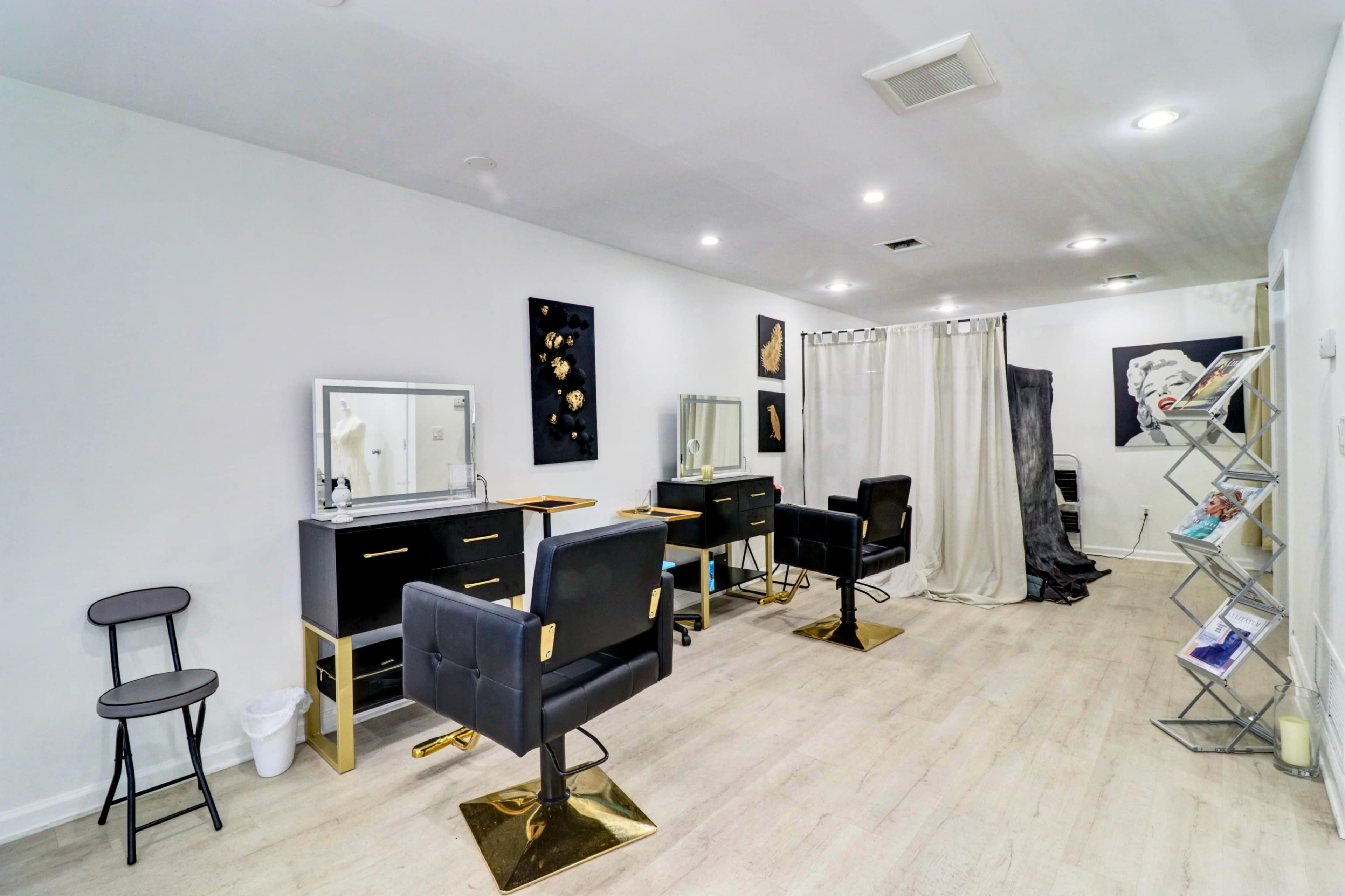 The image shows a modern hair salon with black and gold styling chairs, mirrors, and organized storage on a light-colored wooden floor.