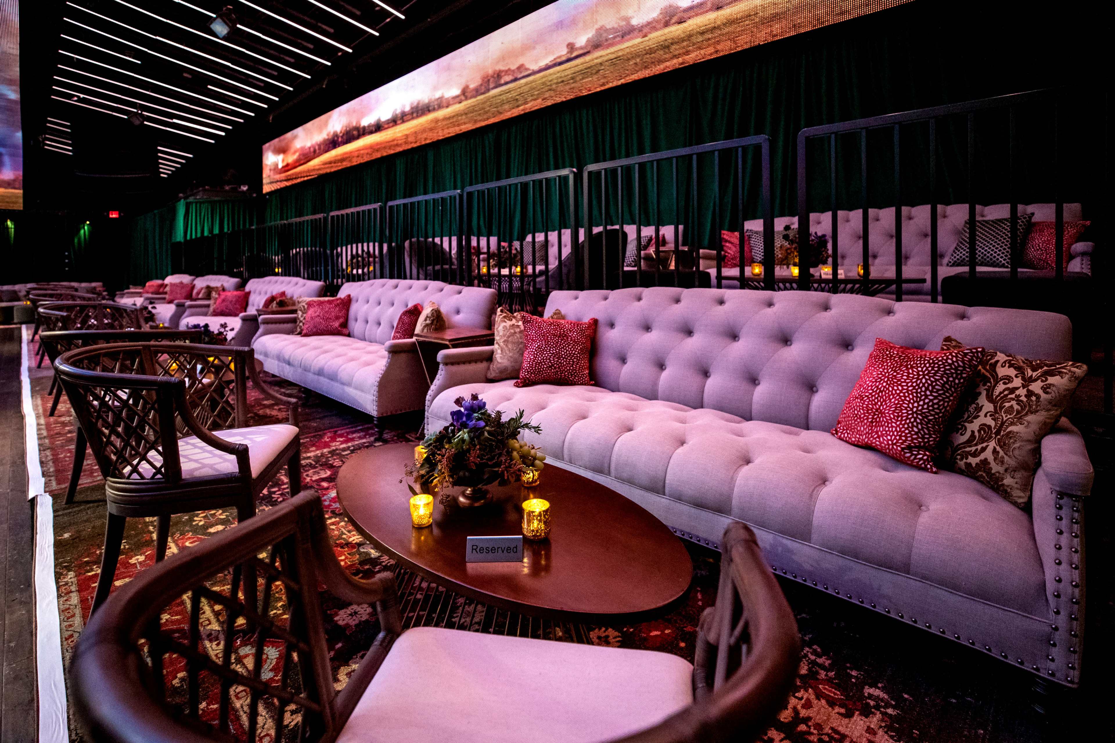 A dimly lit lounge area with plush couches and intimate tables arranged neatly in a seating configuration, complemented by decorative pillows and candles.