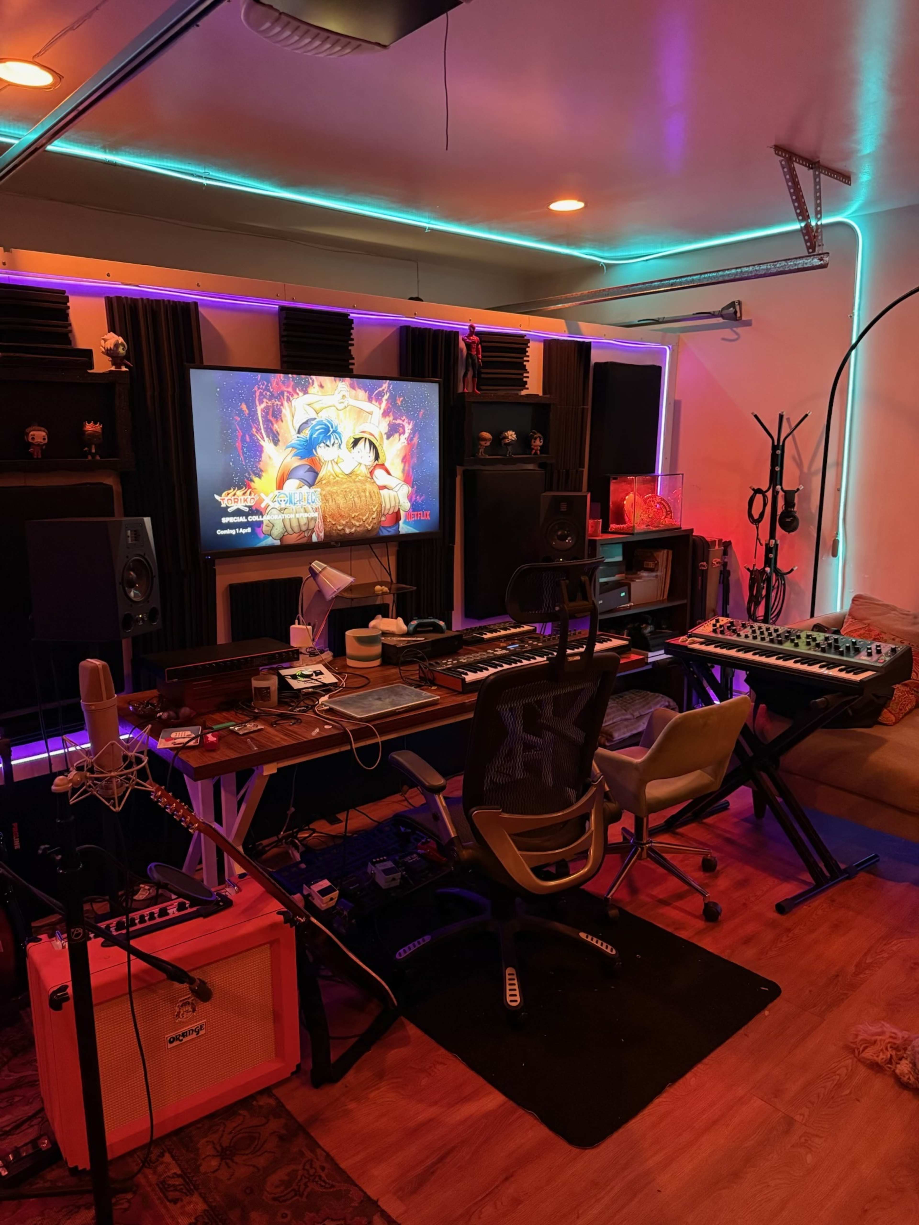 A music studio is equipped with various instruments, audio equipment, and a large screen displaying visuals.