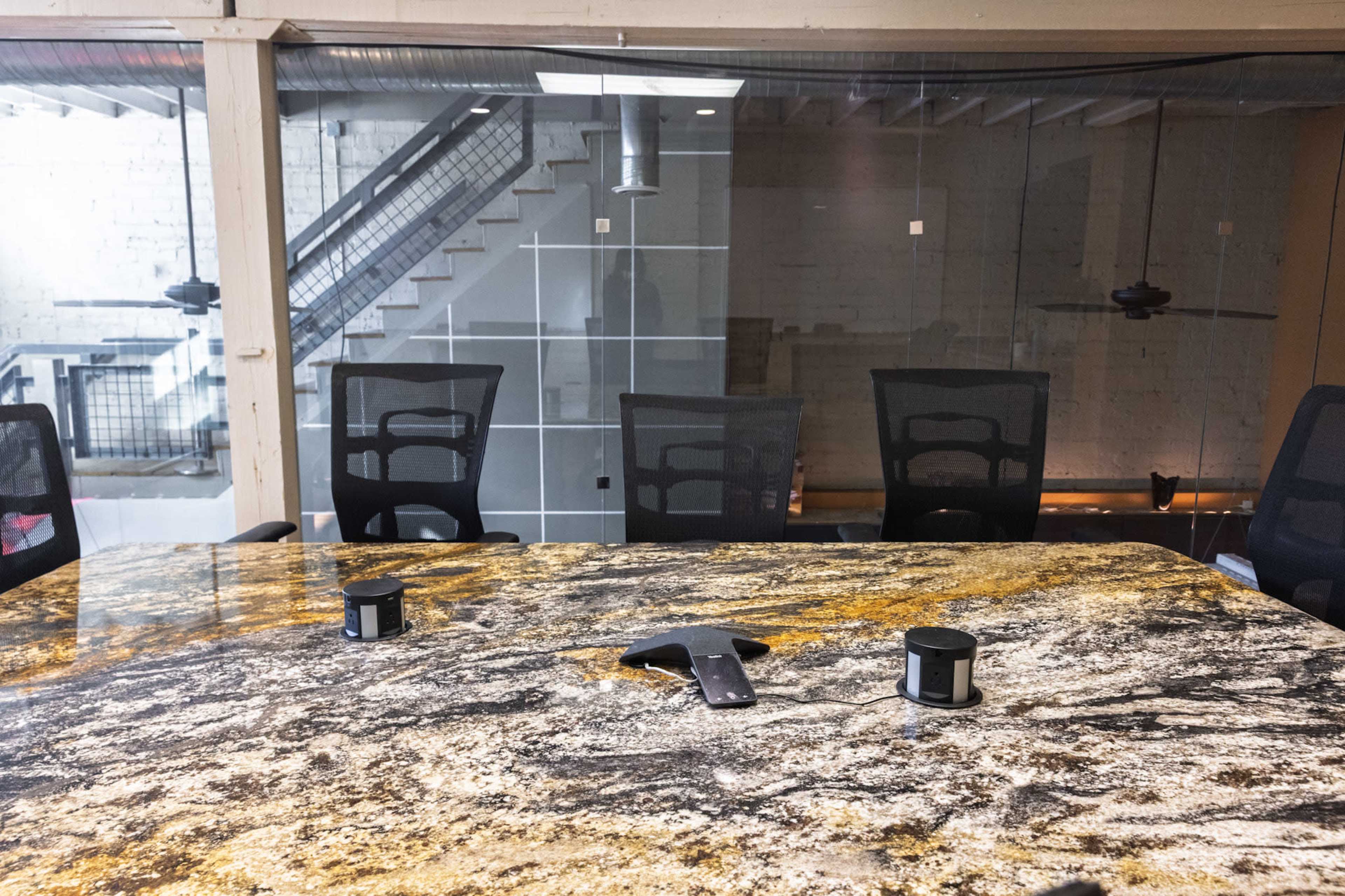 A conference room features a large, textured table with black chairs and a modern glass partition in the background.