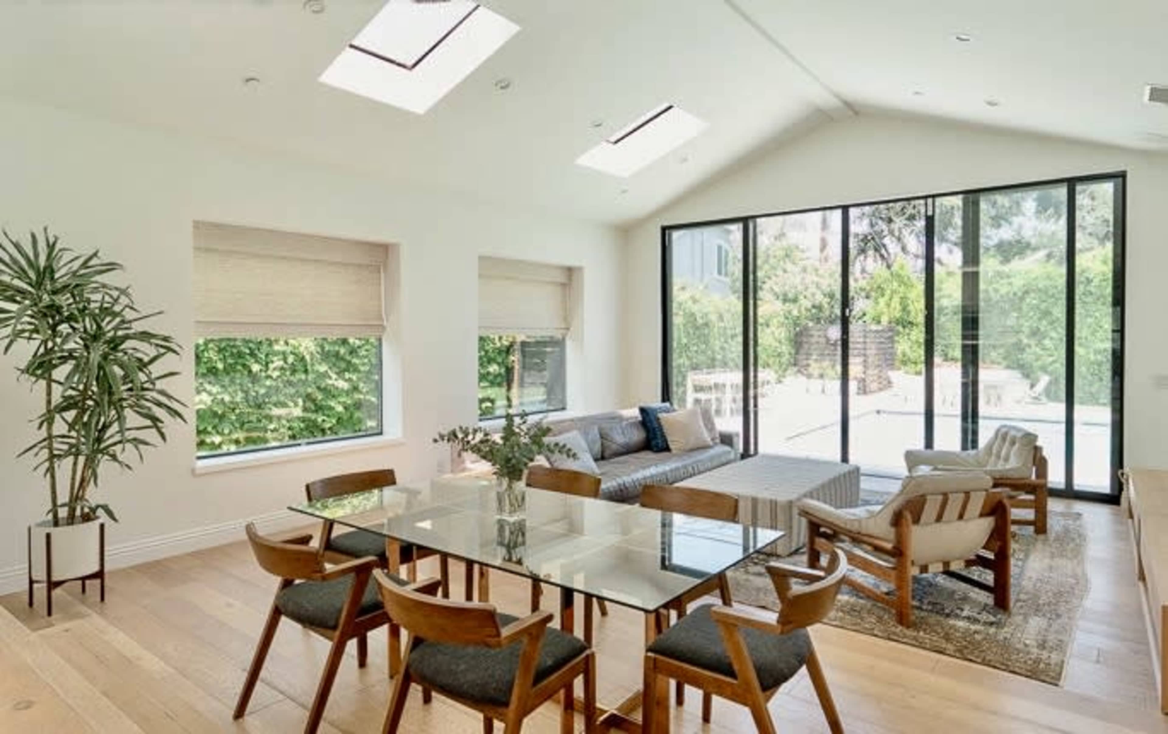 A spacious, modern living area features a glass table surrounded by wooden chairs, large windows, and access to a garden.