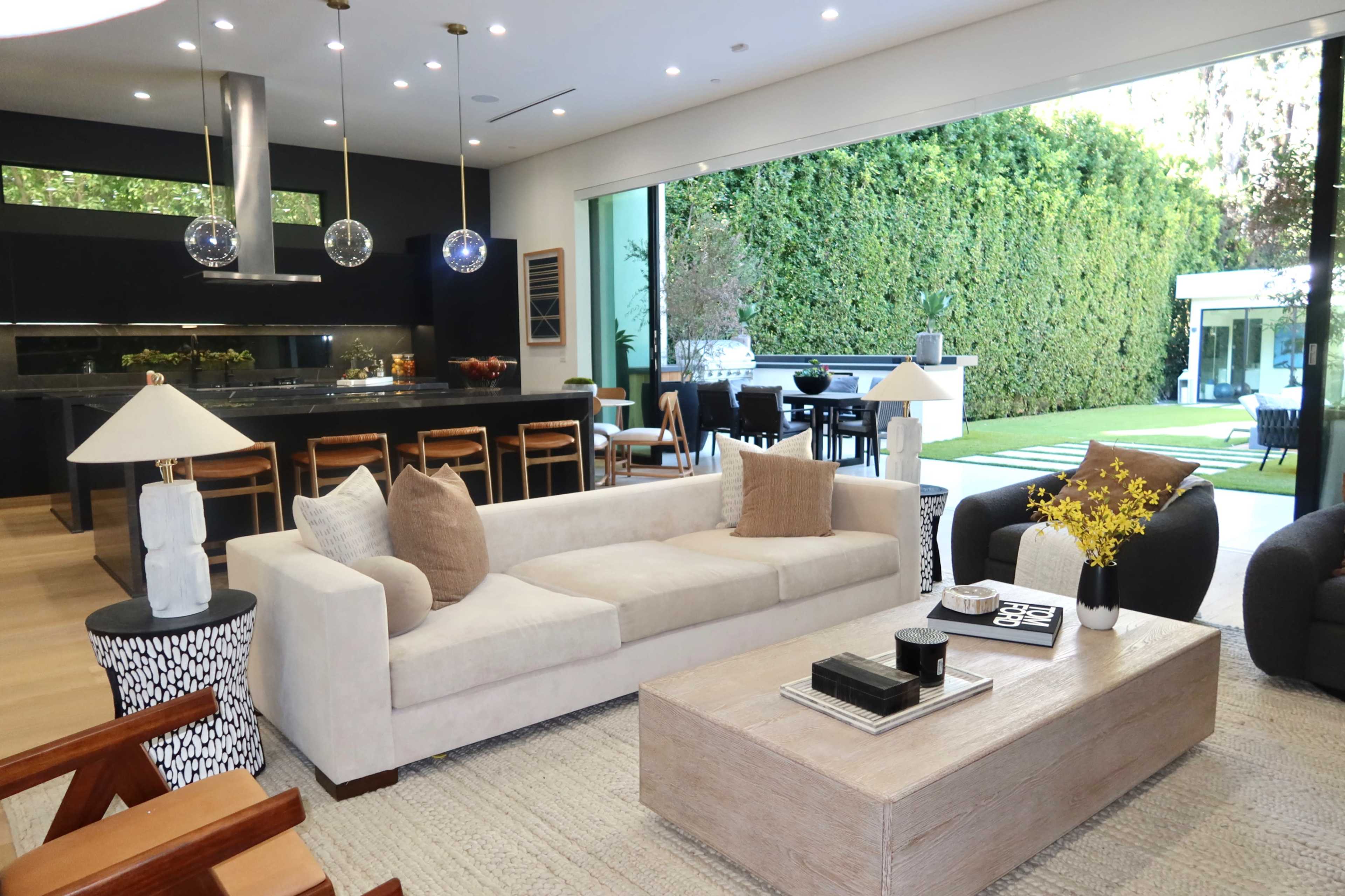 The open-concept living area features a modern design with a beige sofa, a wooden coffee table, and large glass doors that lead to a green outdoor space.