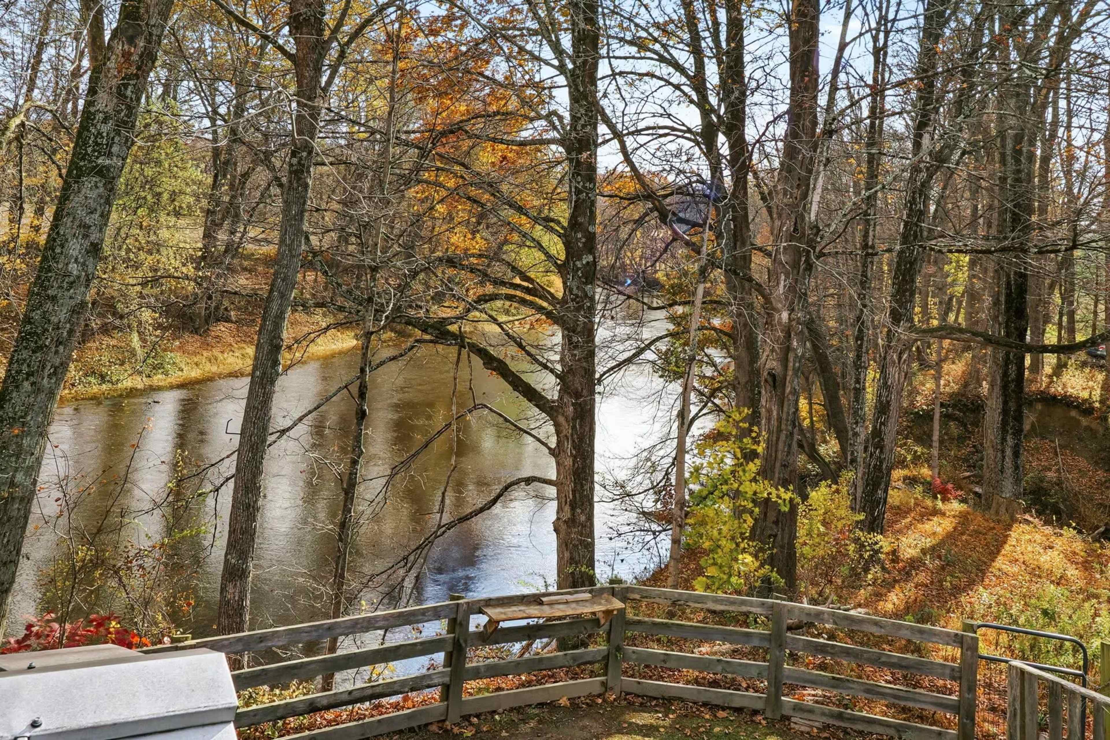 A river flows gently through a wooded area with trees featuring autumn foliage.