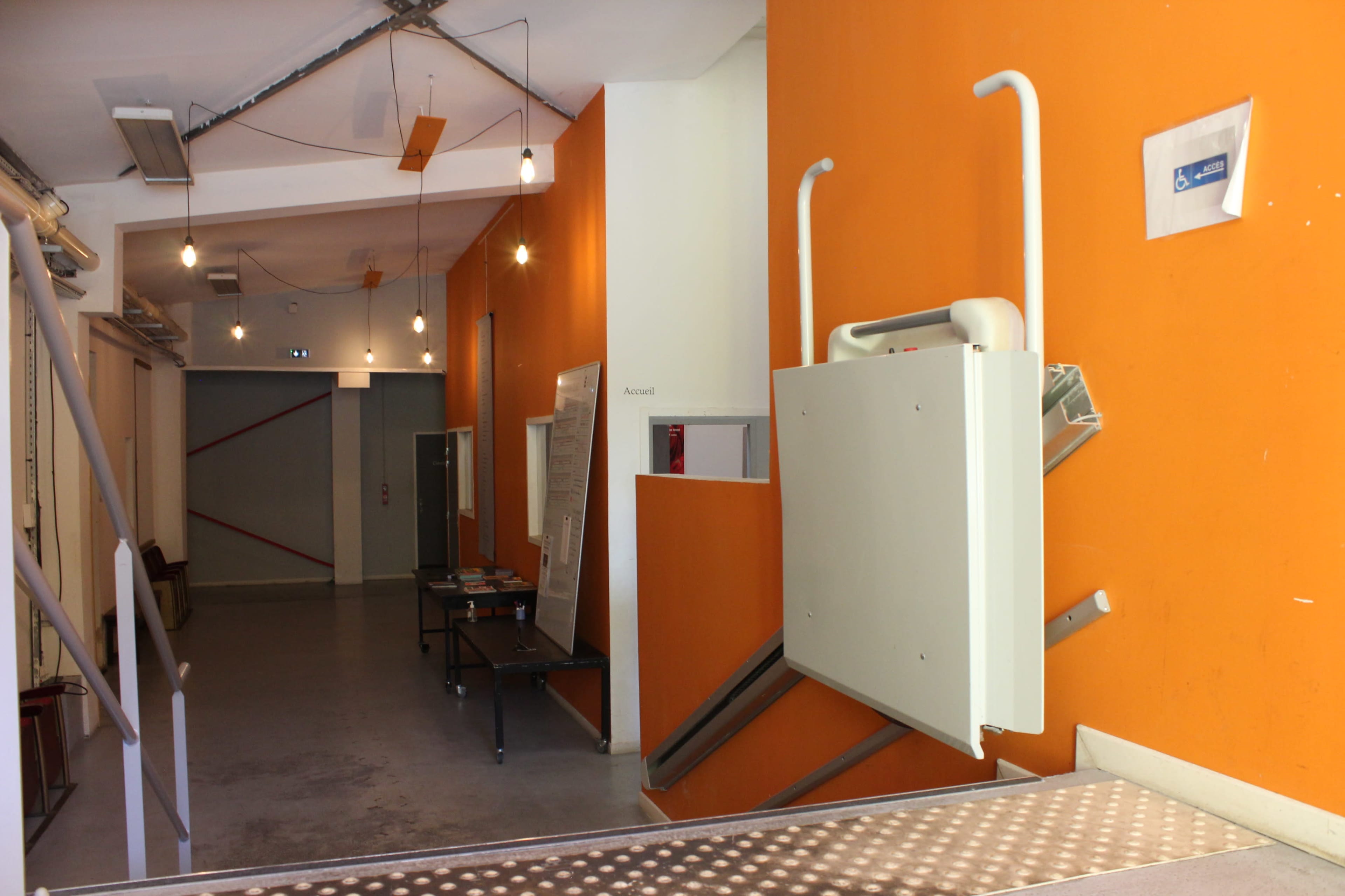 A hallway with an orange wall, a ramp for accessibility, and a table against the opposite wall.