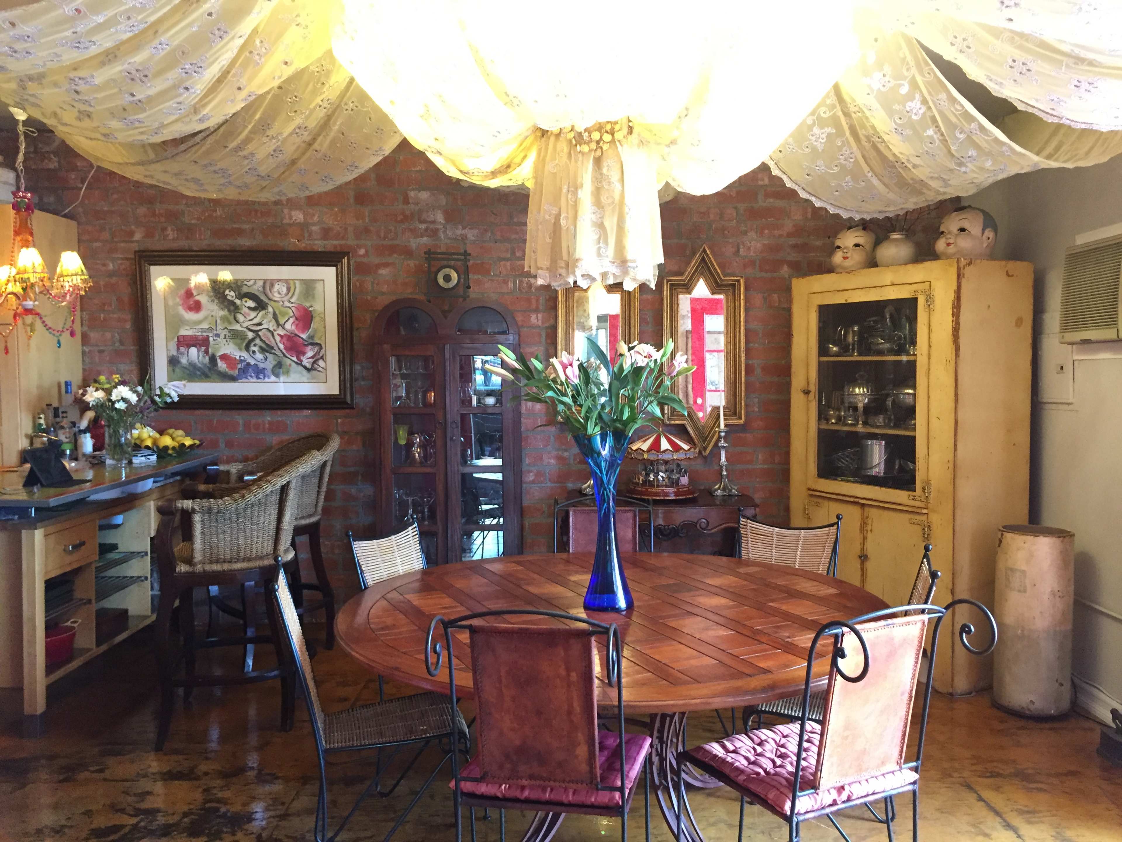 A cozy dining area with a wooden table, surrounded by various chairs, and decorated with a large draped fabric ceiling and vintage furnishings.