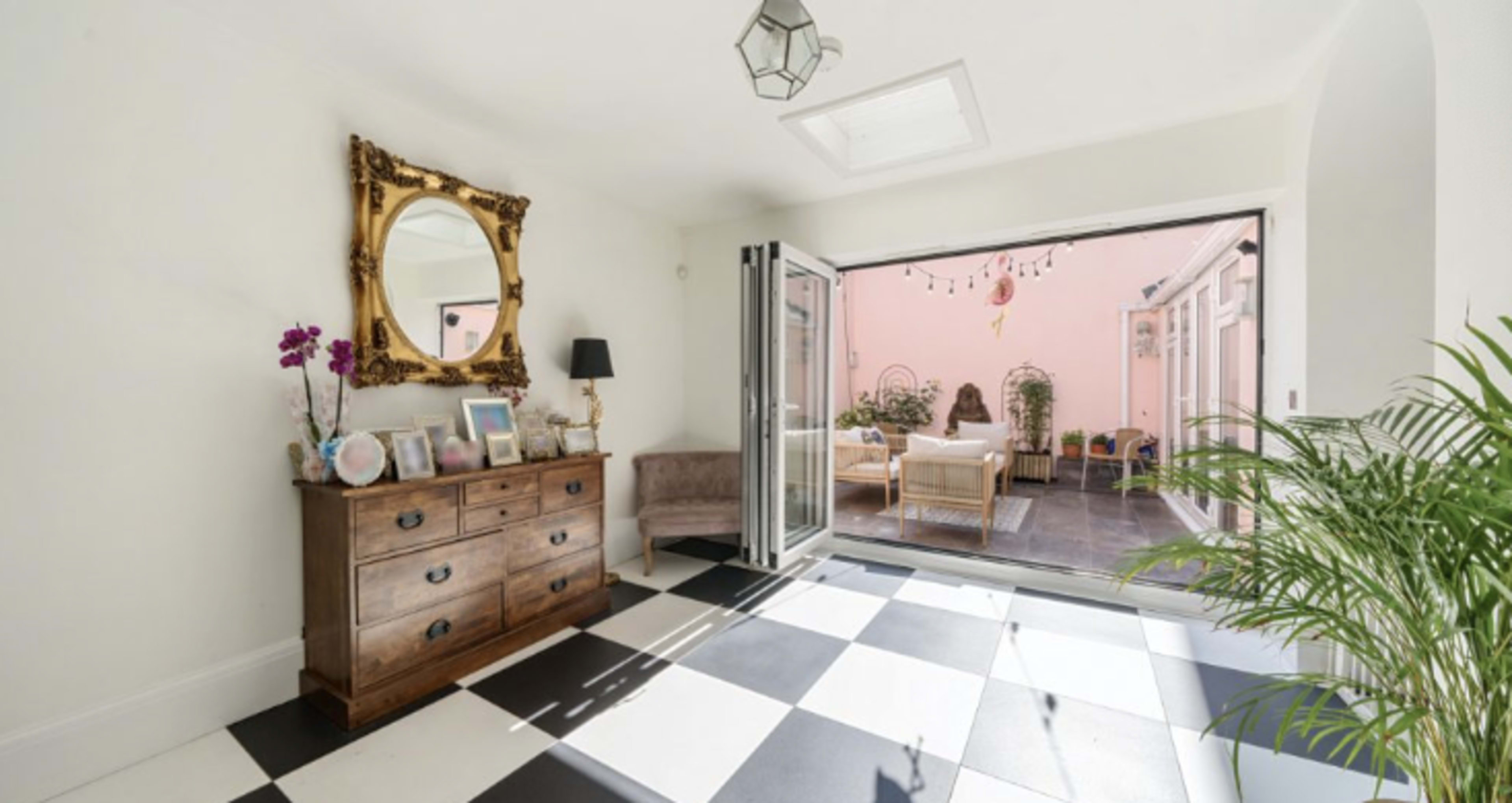 A bright entryway with black and white checkered flooring, a wooden chest of drawers, a round mirror, and sliding glass doors leading to a patio.