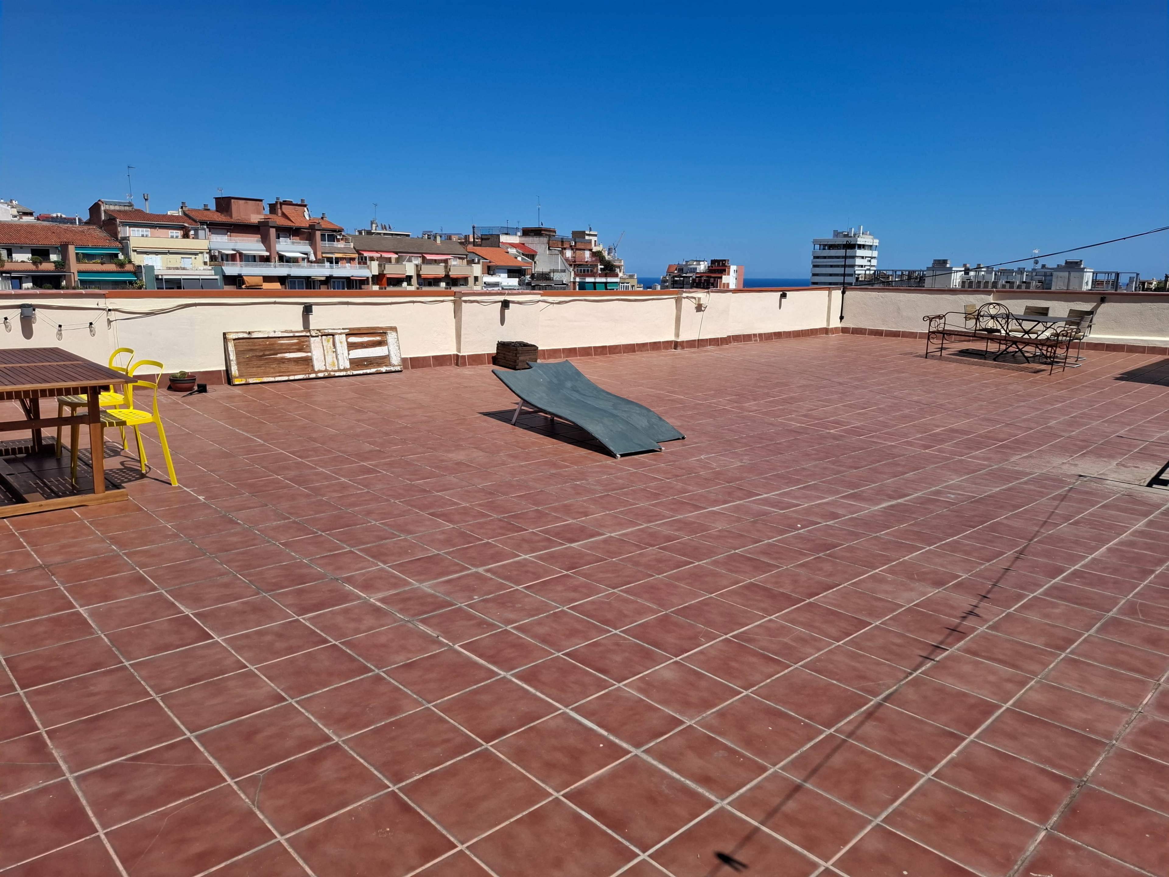 The image shows a spacious rooftop terrace with red tiles, featuring a sloped surface in the center and several structures in the background.
