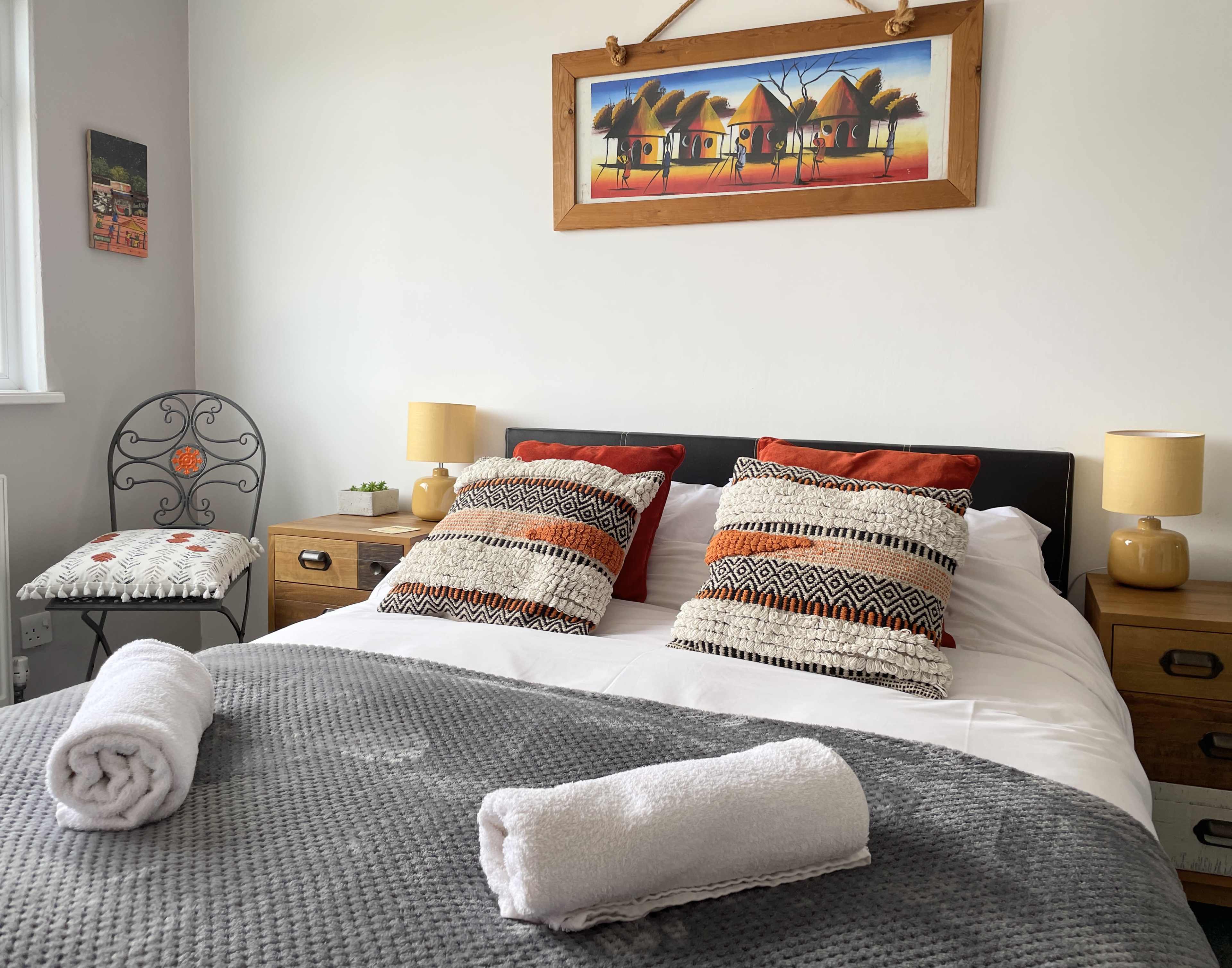 A neatly made bed with decorative pillows, two bedside lamps, and an artwork hanging above, set in a well-lit bedroom.