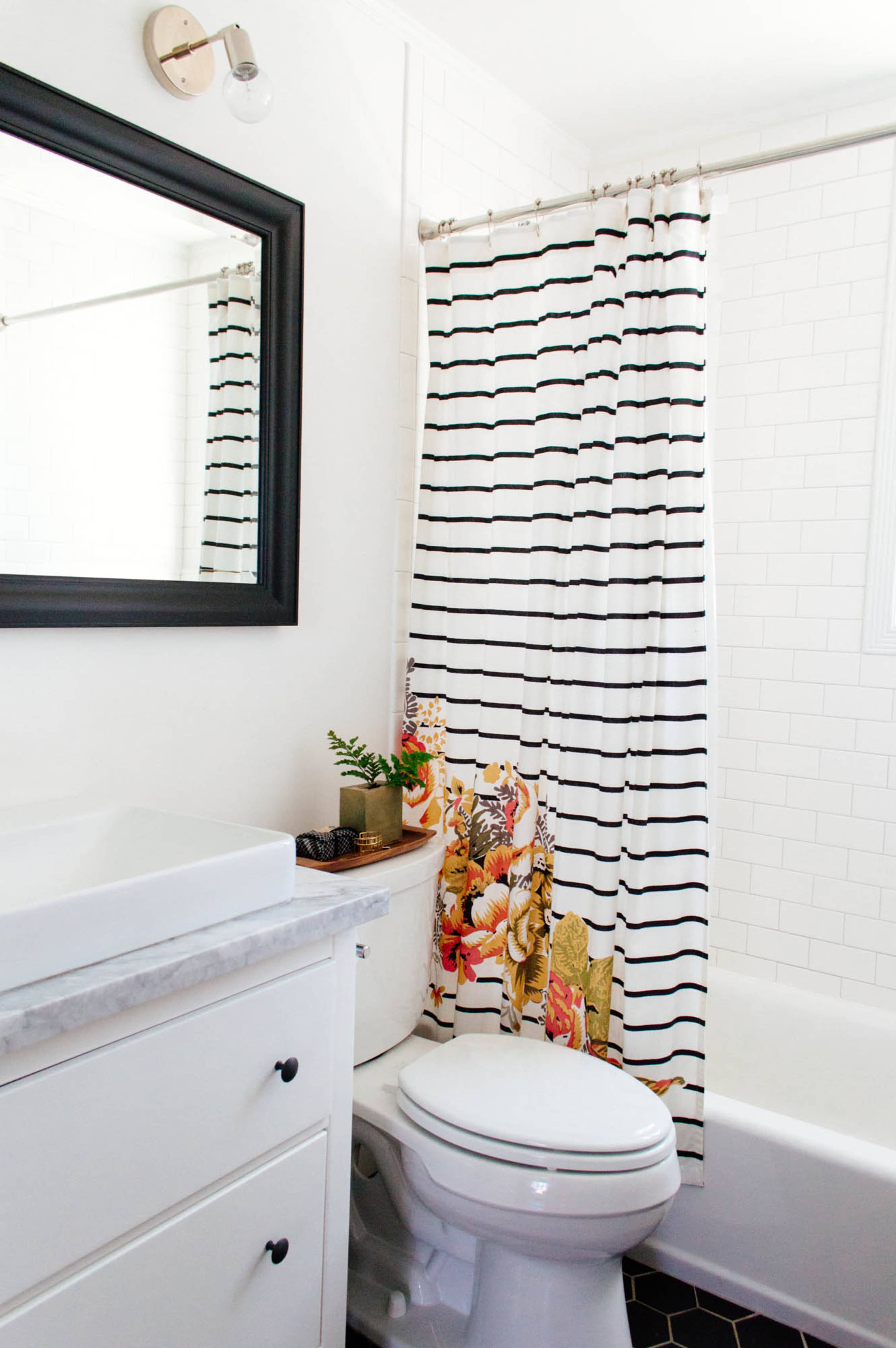 A bathroom with a white tiled wall, a black framed mirror, a striped shower curtain, and a toilet next to a sink with a marble countertop.