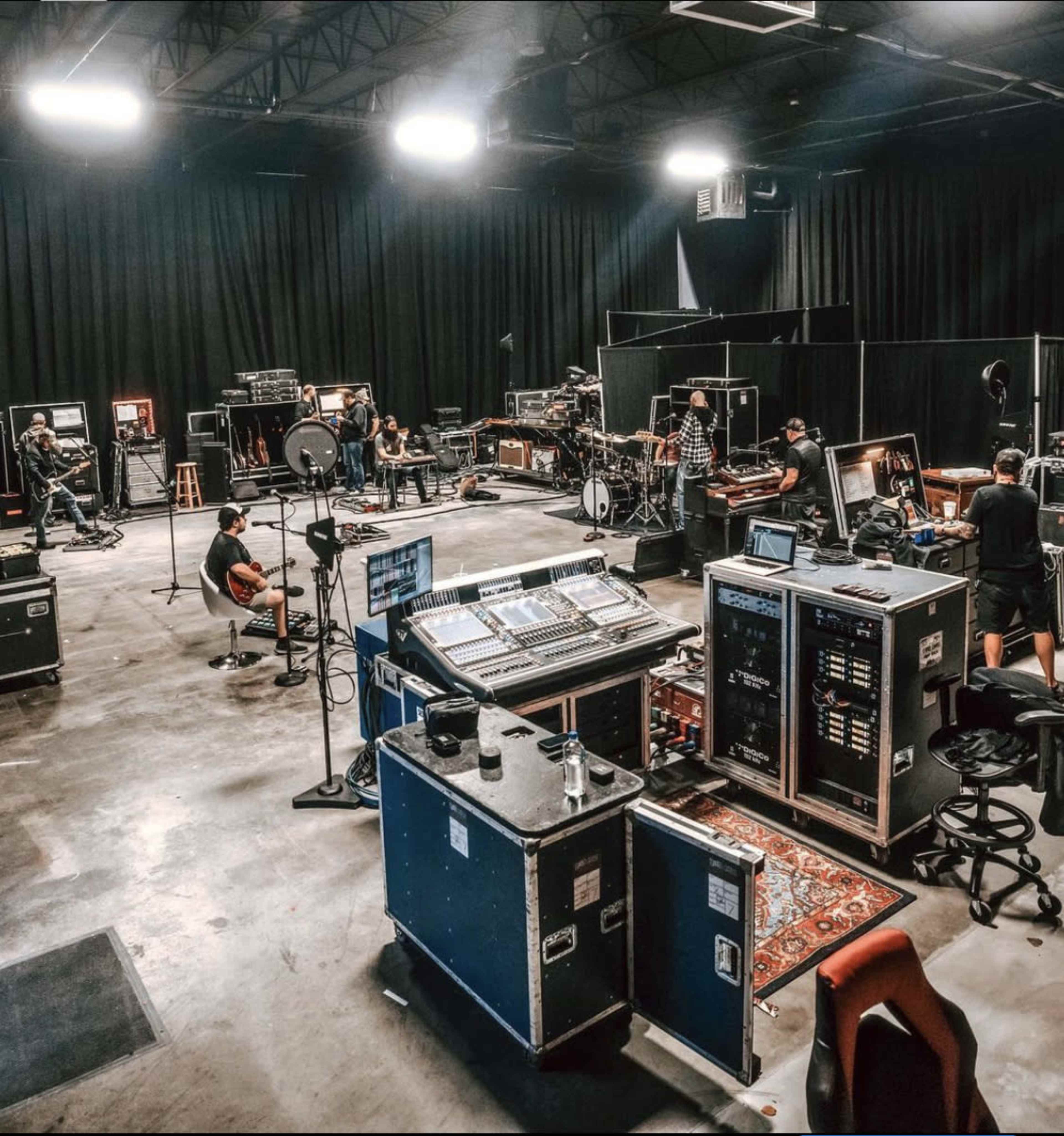 A group of musicians and technicians work in a spacious rehearsal studio equipped with sound and lighting equipment.