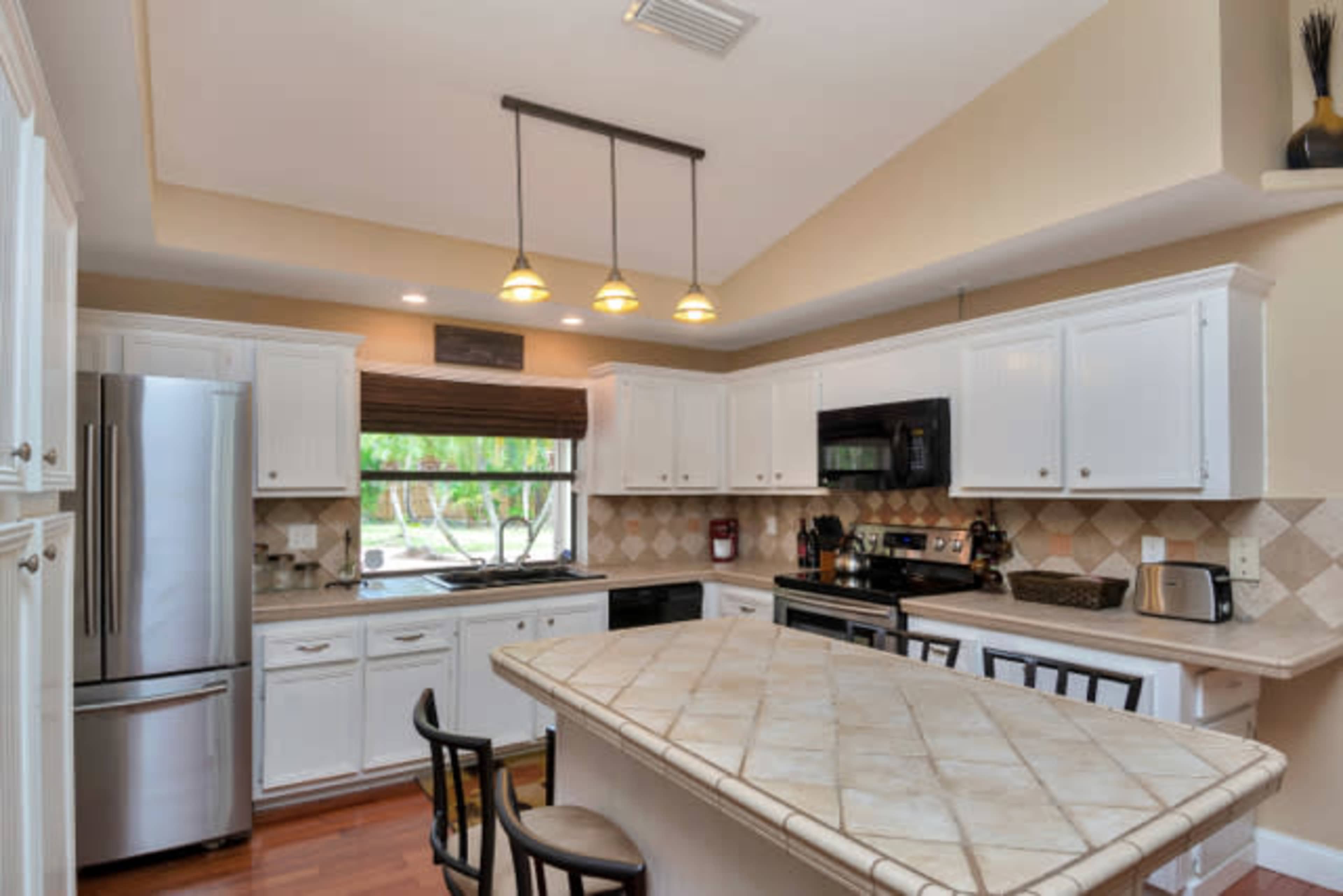 A modern kitchen features white cabinetry, stainless steel appliances, and a tile countertop with an island and seating.