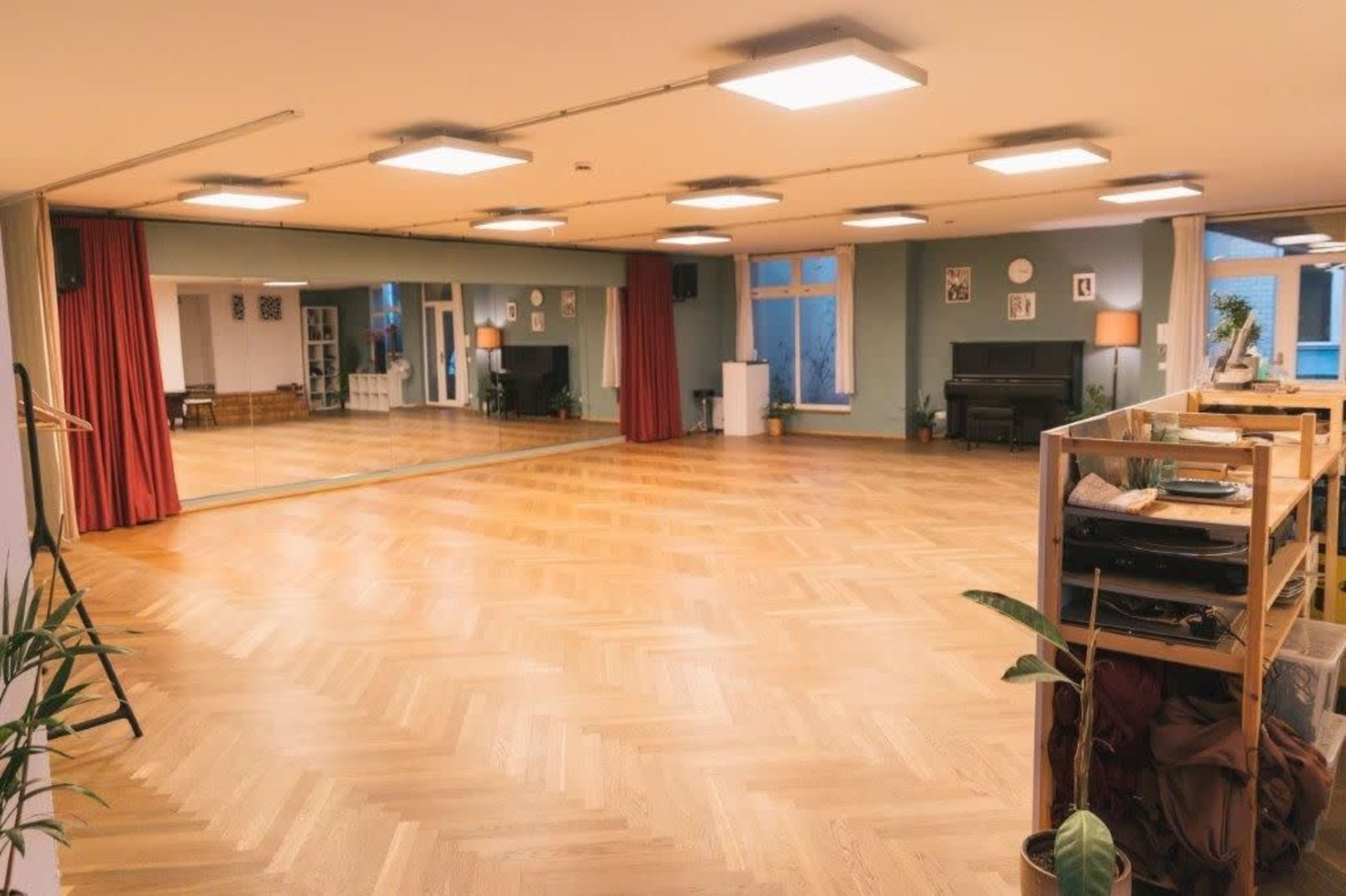 The image shows a spacious dance studio with wooden flooring, large mirrors on one wall, and soft lighting.