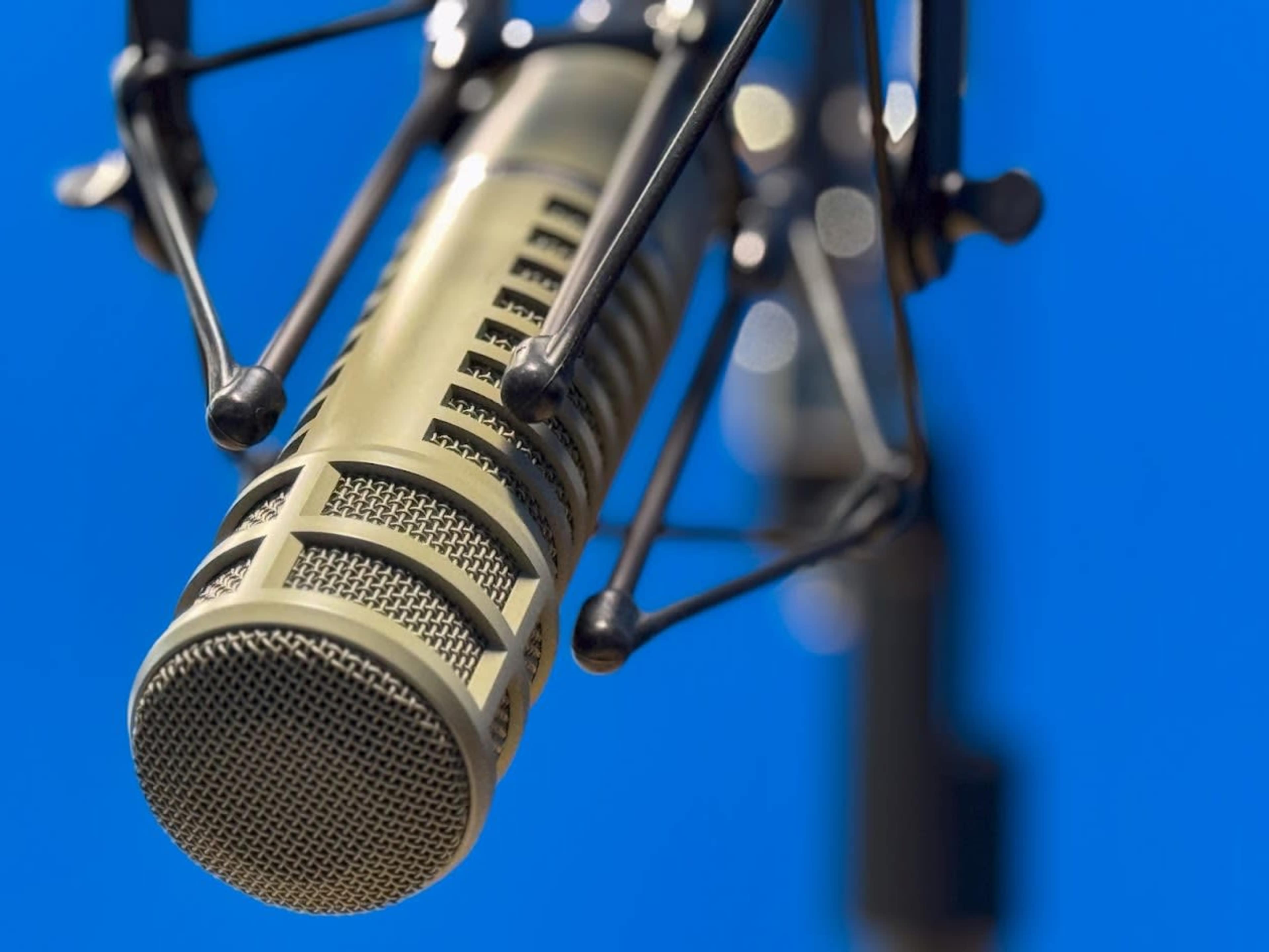 A close-up image of a microphone against a clear blue background.