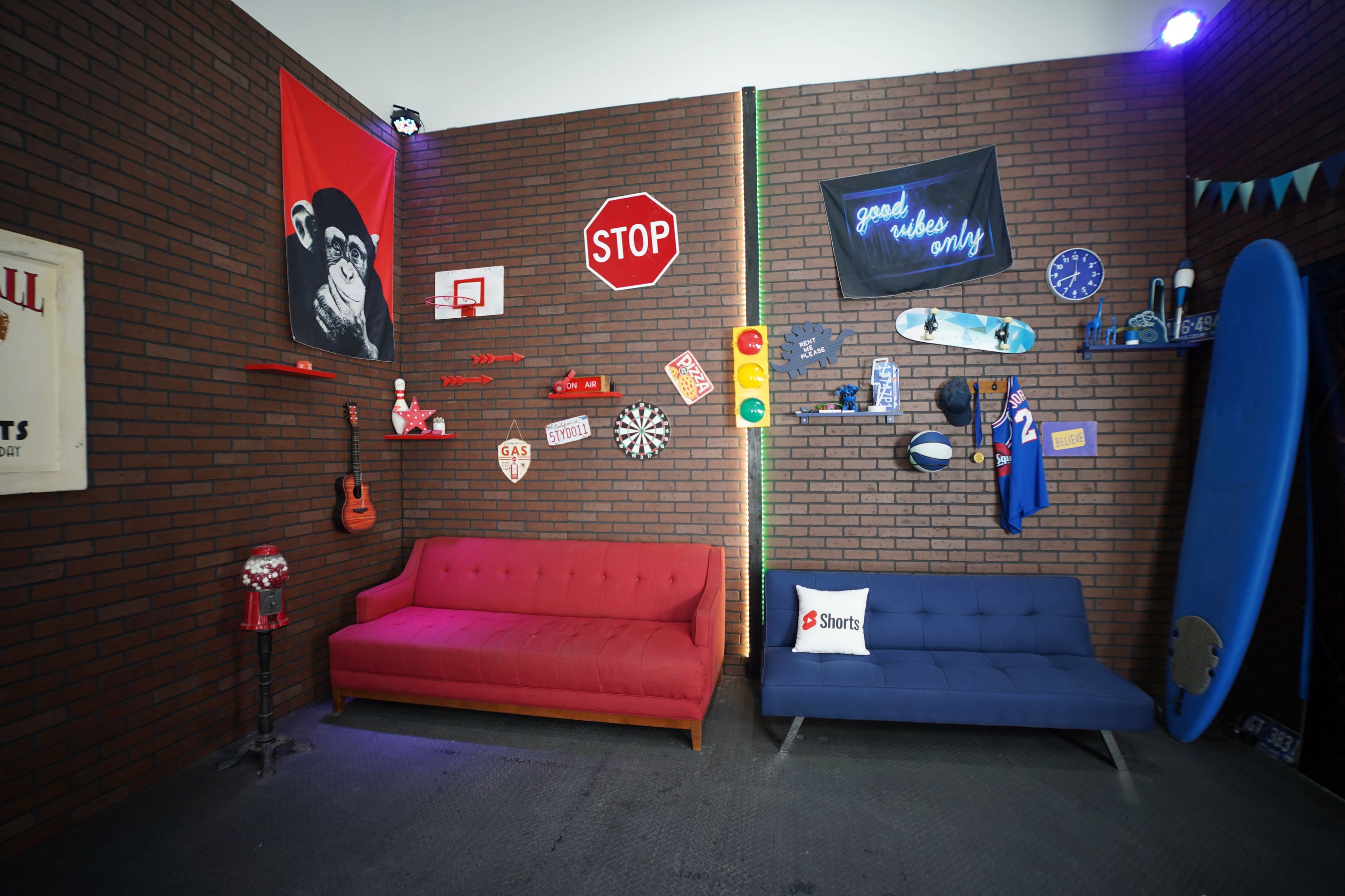 The scene features a brick-walled room with two sofas, various wall decorations including a stop sign, a surfboard, and colorful signage.