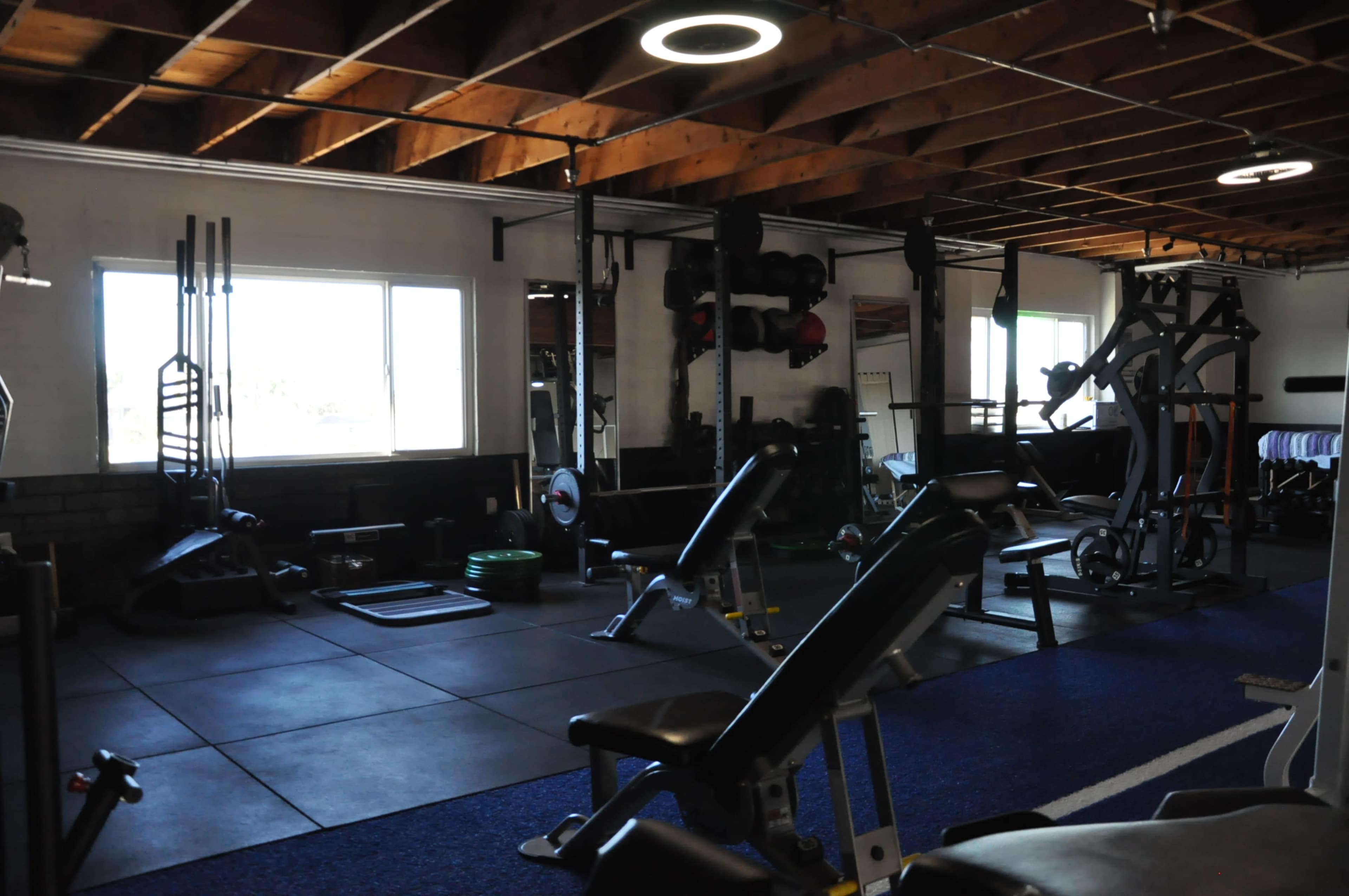 A gym interior with various exercise equipment, including weight benches and resistance machines, under a wooden ceiling.