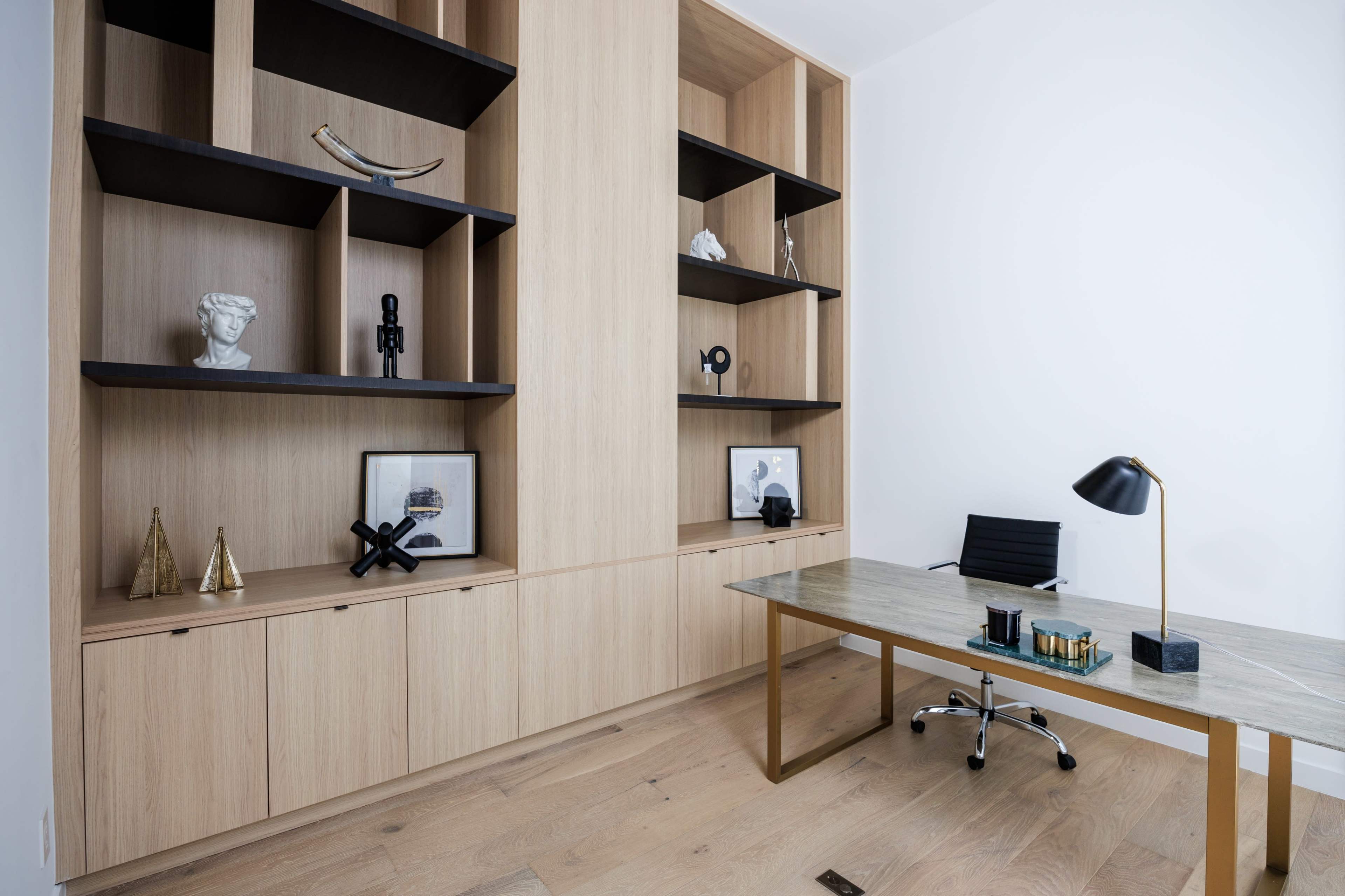 The image shows a modern office space featuring a large wooden shelving unit, a glass-top desk with a metal base, and minimalistic decor.
