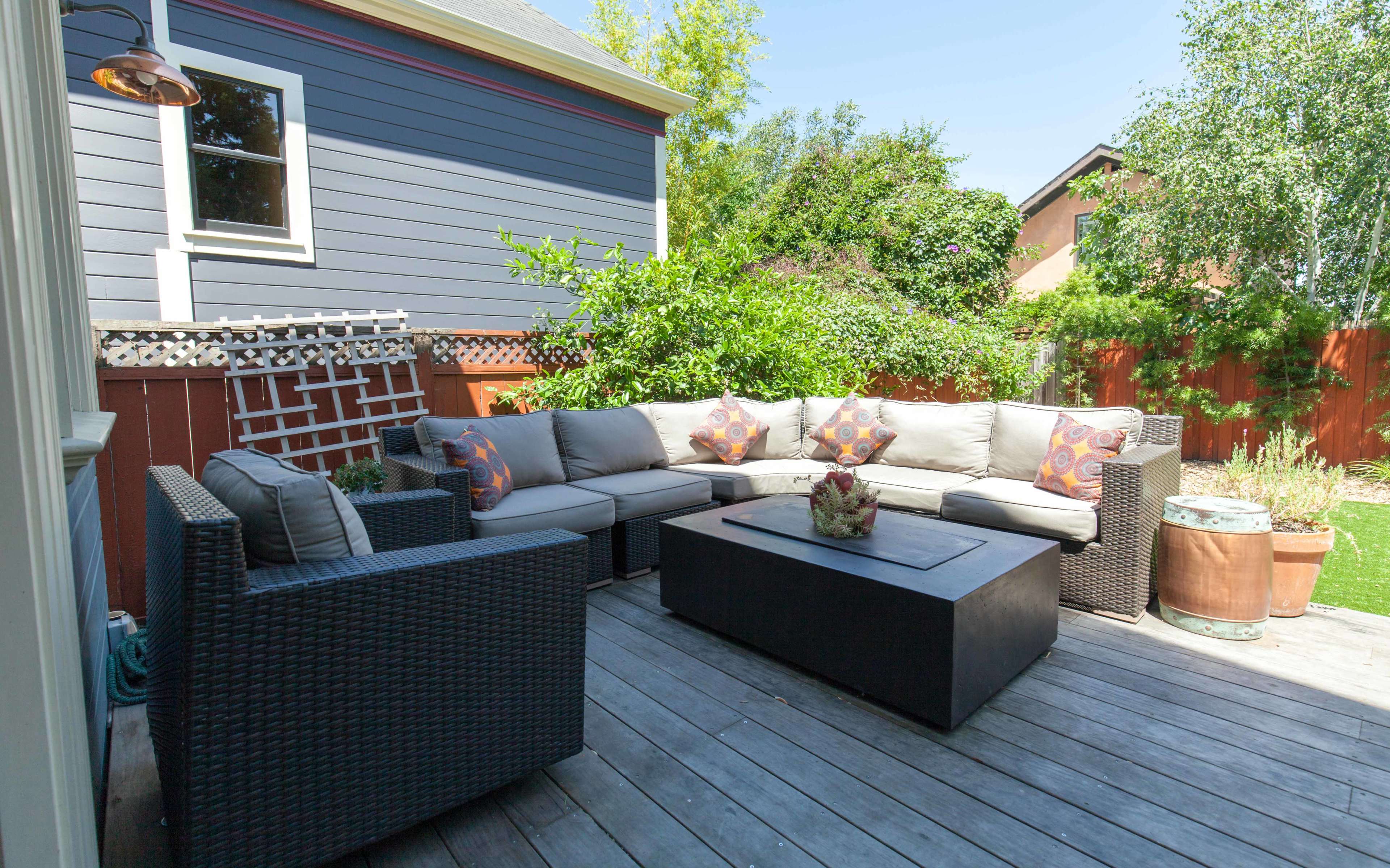 A spacious outdoor seating area features a sectional sofa and a coffee table on a wooden deck surrounded by greenery.