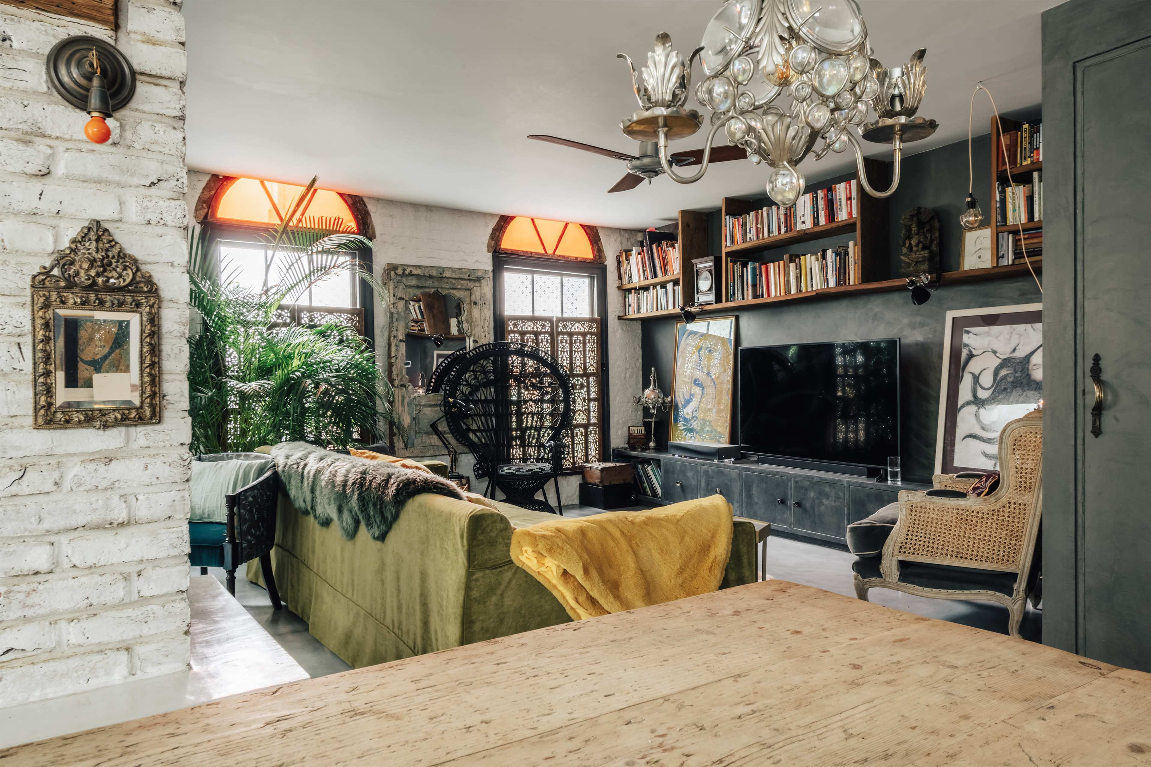 The image shows a cozy living room with a green couch, bookshelves, and large windows adorned with decorative elements.
