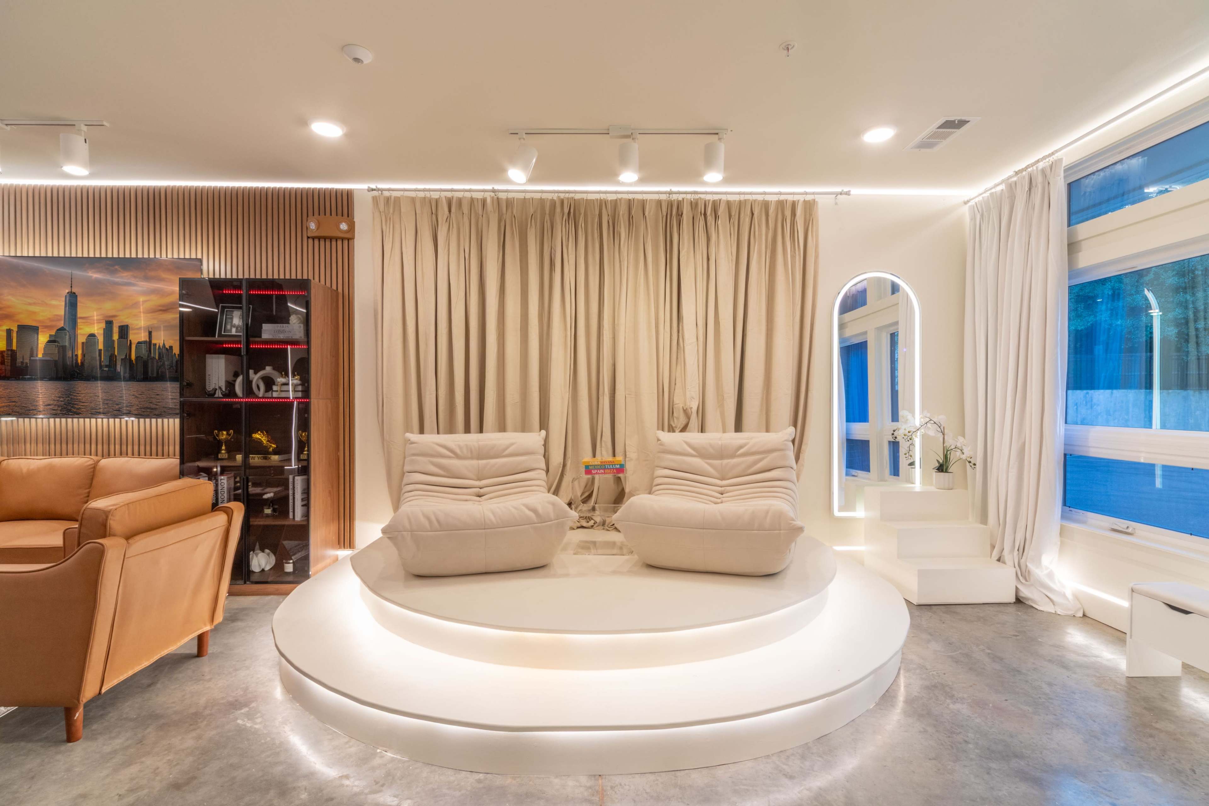 The image depicts a modern interior design featuring two large, cushioned chairs on a circular platform, with a backdrop of flowing curtains and ambient lighting.