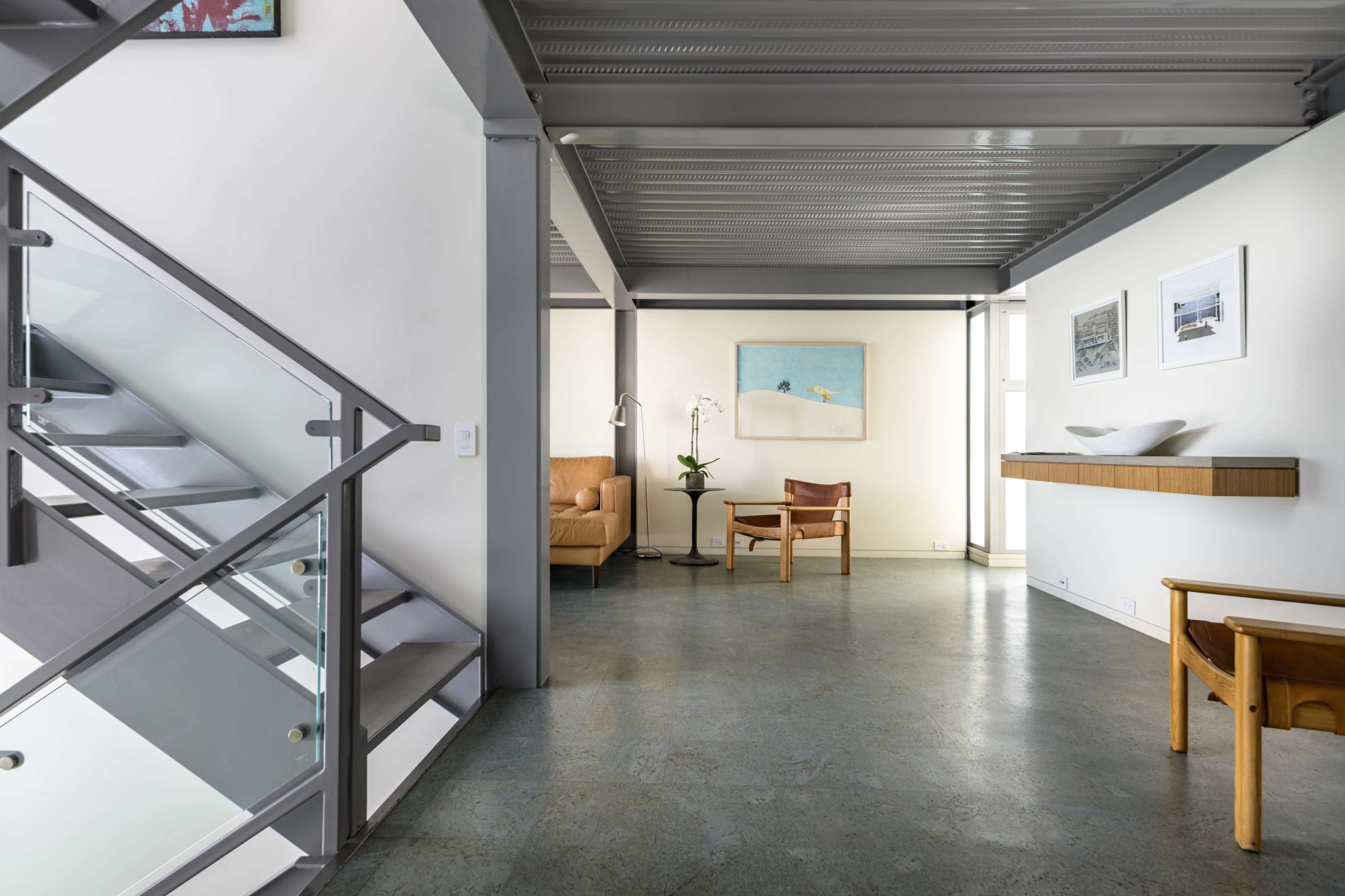 A modern interior space featuring a staircase, a seating area with a chair and side table, and wall art.