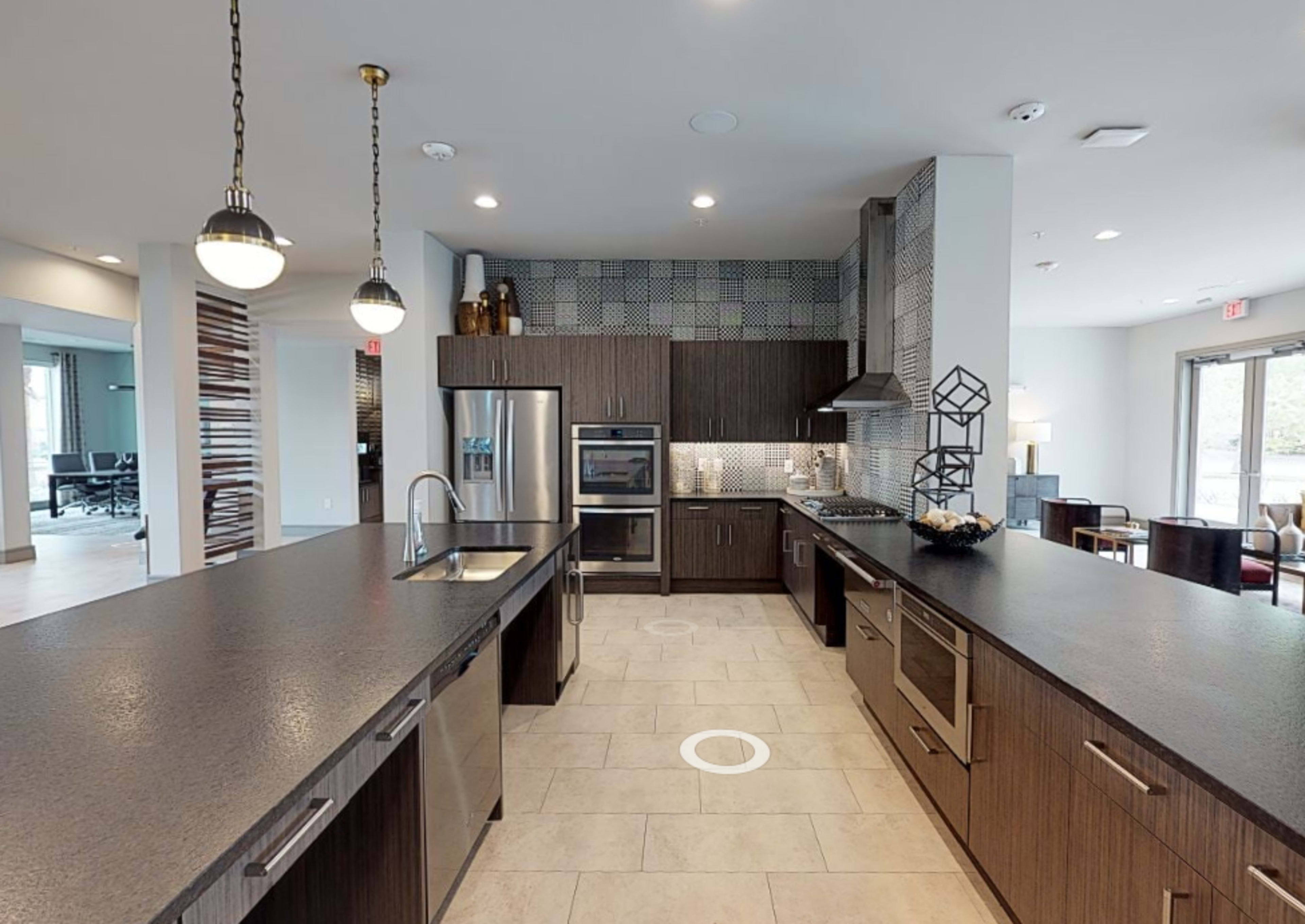 A modern kitchen with dark cabinetry, stainless steel appliances, and a tiled backsplash, featuring an island with a sink.