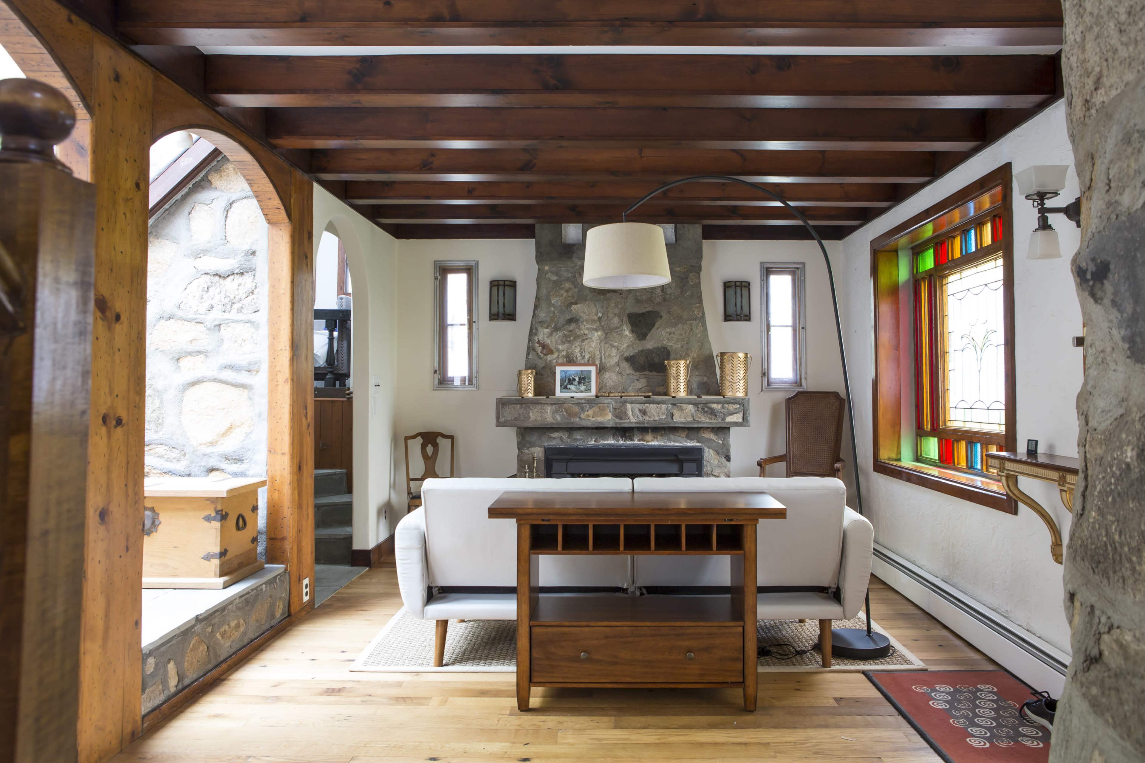 The living room features a stone fireplace with a wooden mantel, a white couch, and a colorful stained glass window.