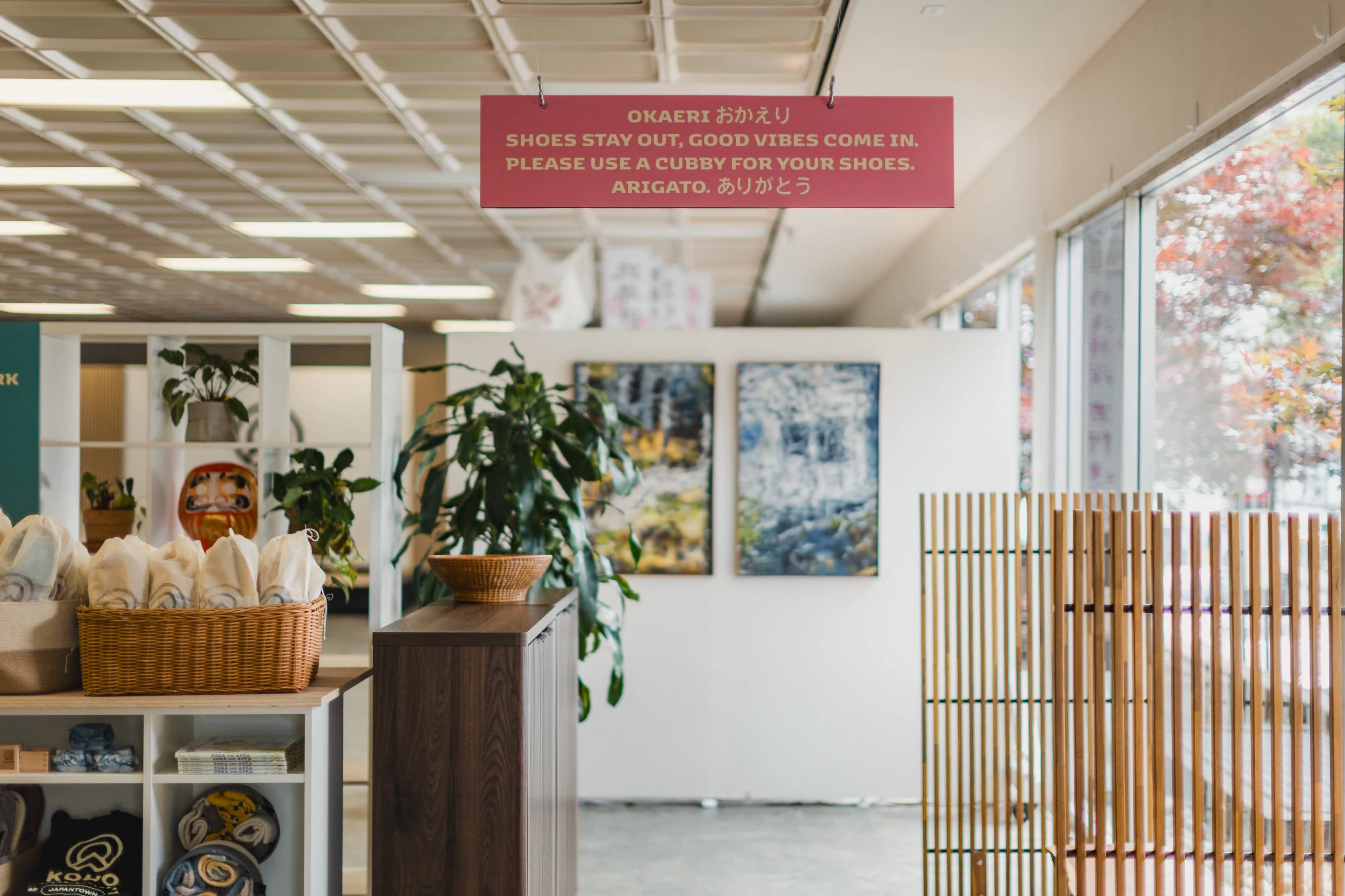 The interior of a welcoming space features a sign in multiple languages about removing shoes, alongside shelves with baskets and artwork on the walls.