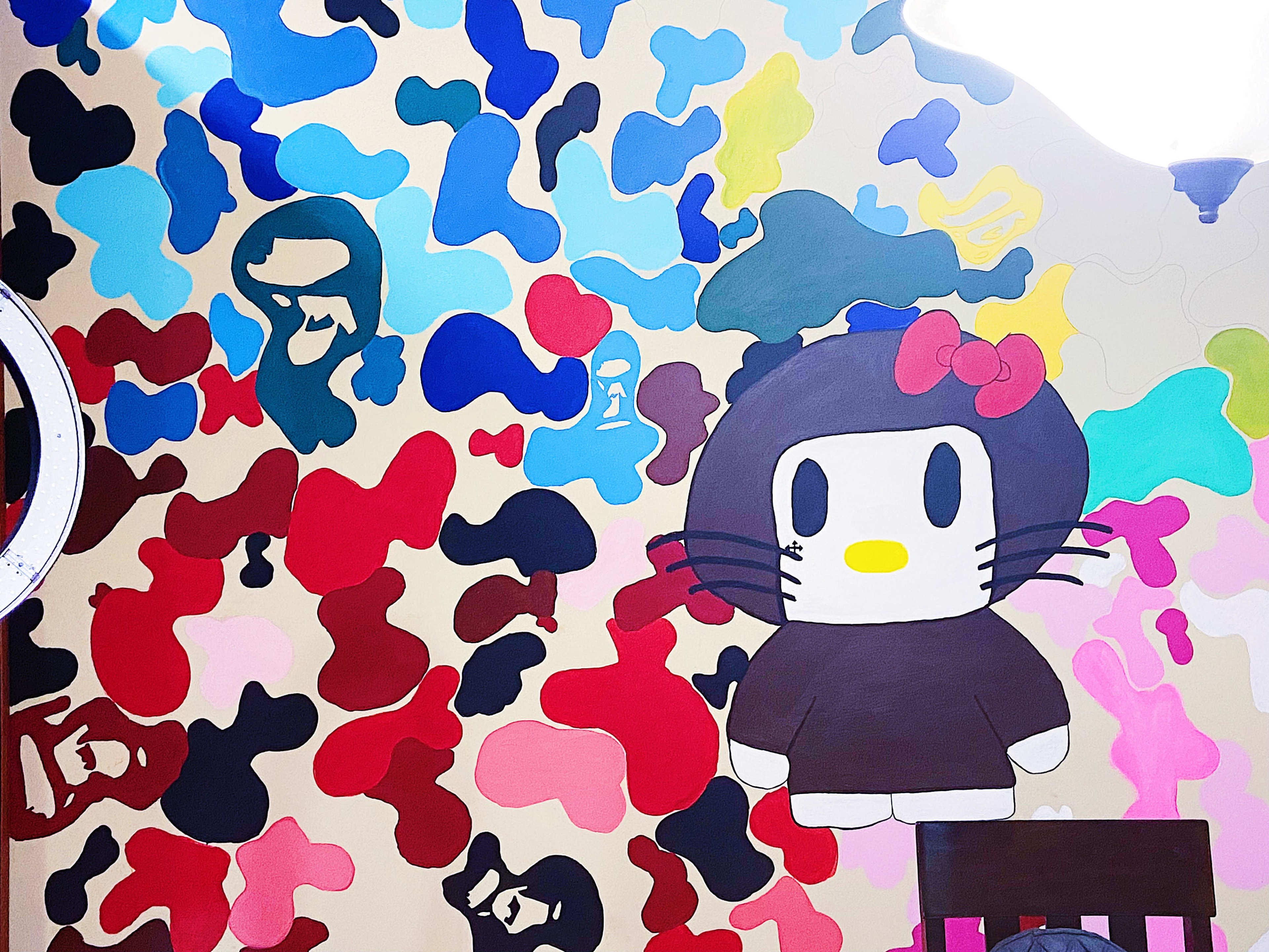 The image features a colorful mural on a wall, prominently displaying a cartoon character resembling Hello Kitty amidst various abstract shapes and colors.