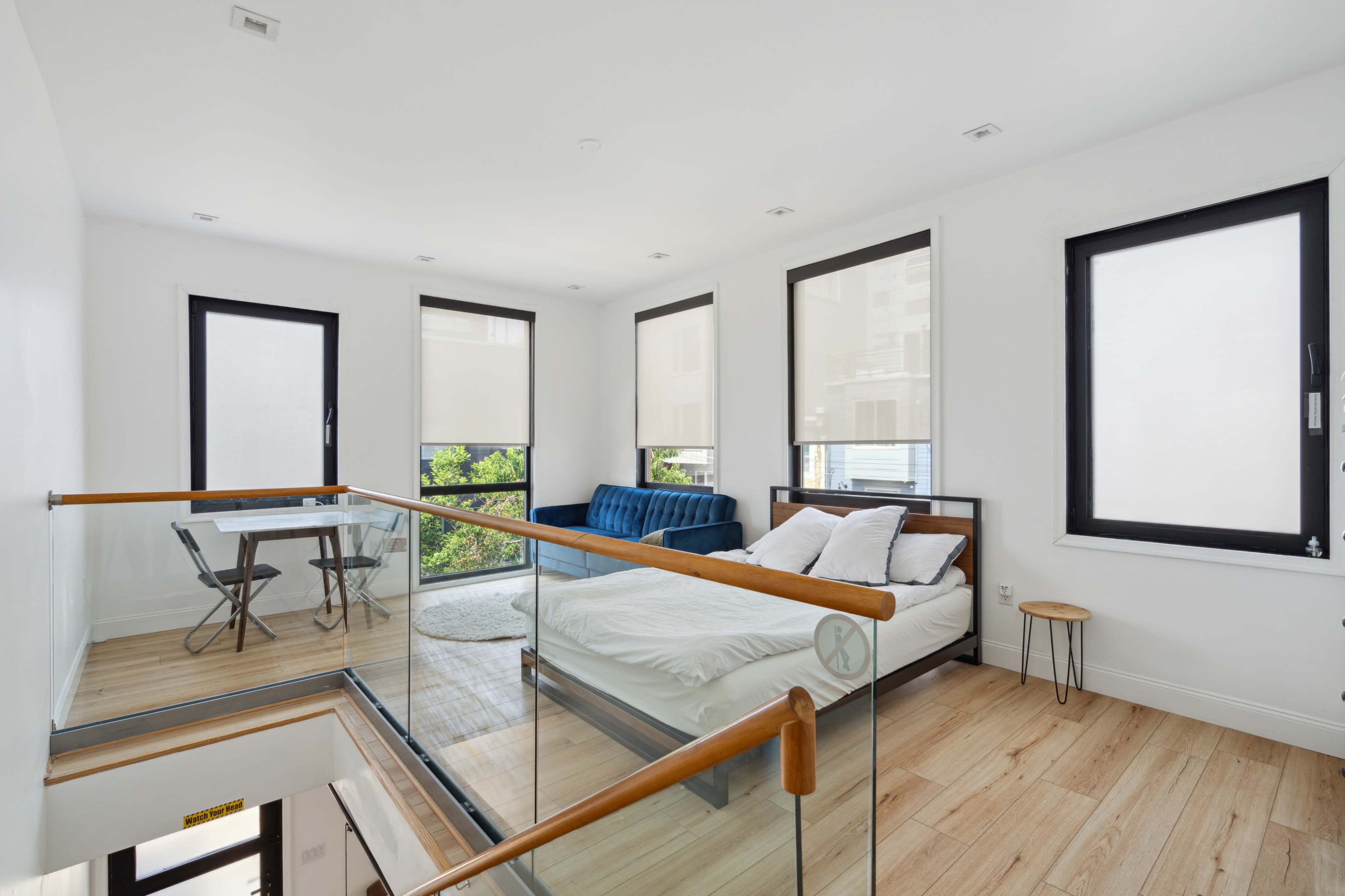 The image shows a modern, open-concept bedroom and seating area with large windows and a wooden floor.