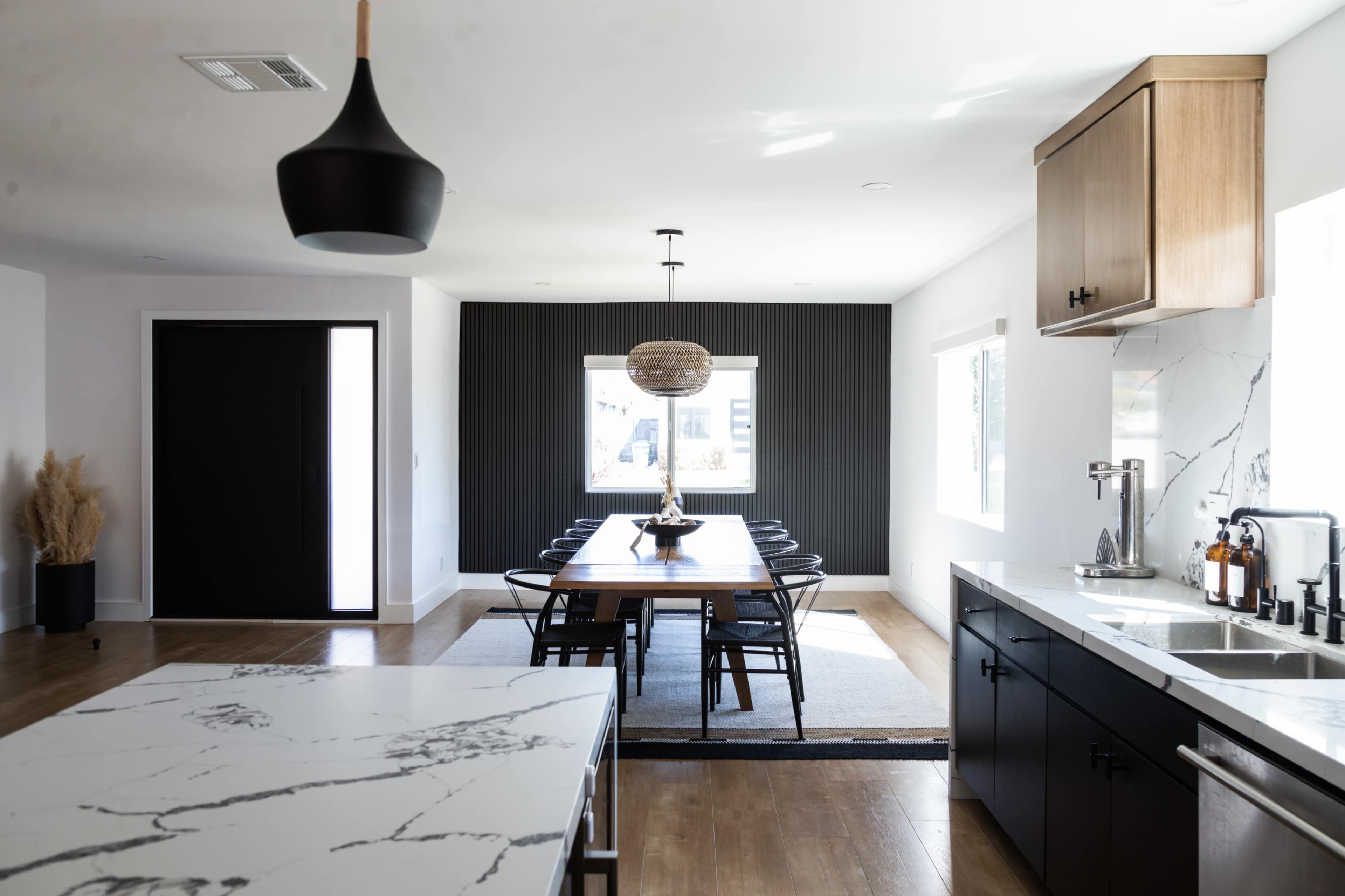 A modern kitchen area features a marble countertop island and a dining table surrounded by black chairs, with a large window illuminating the space.