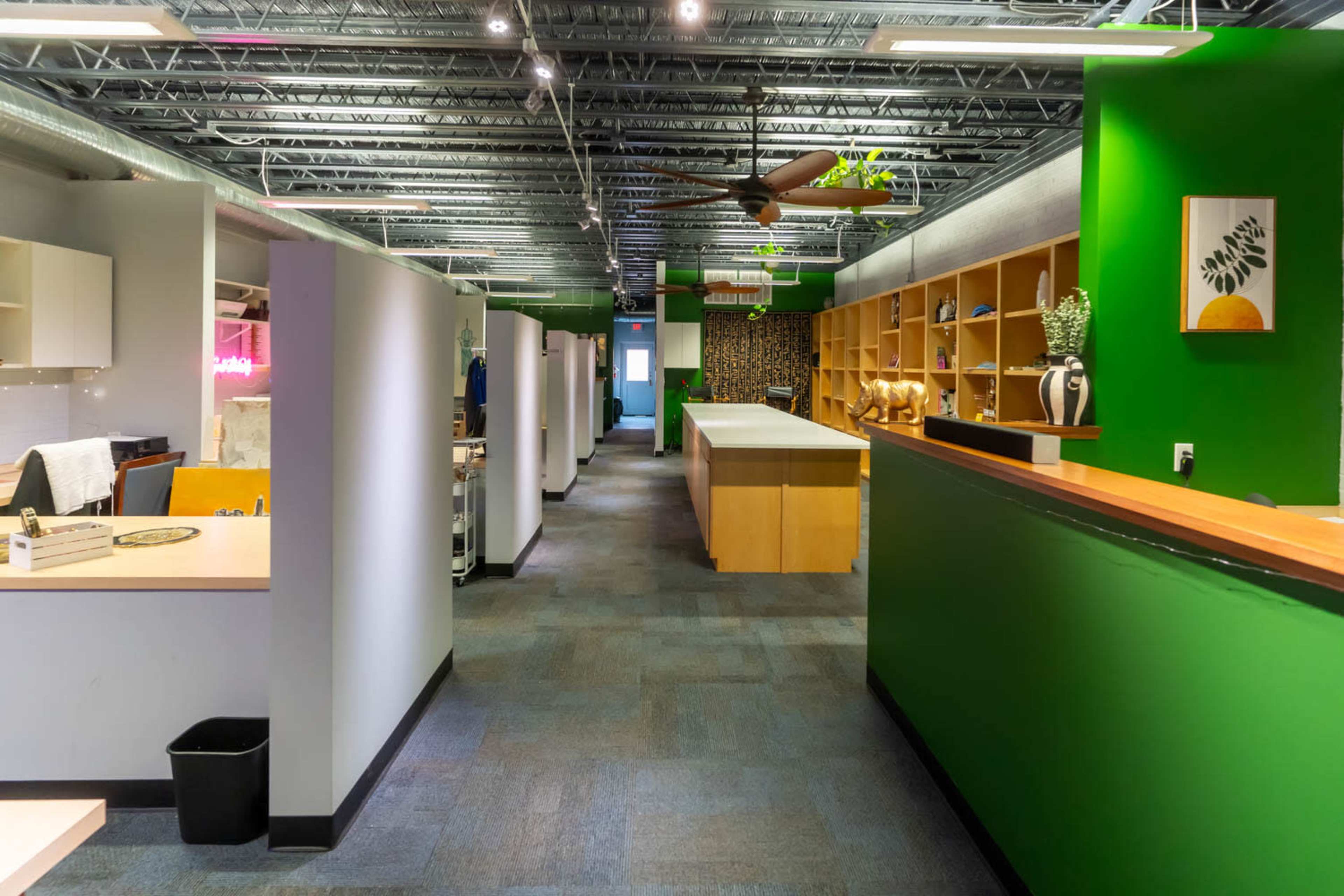 A modern office interior with green walls, wooden shelves, and a long reception desk, with workstations and open spaces lining the hallway.