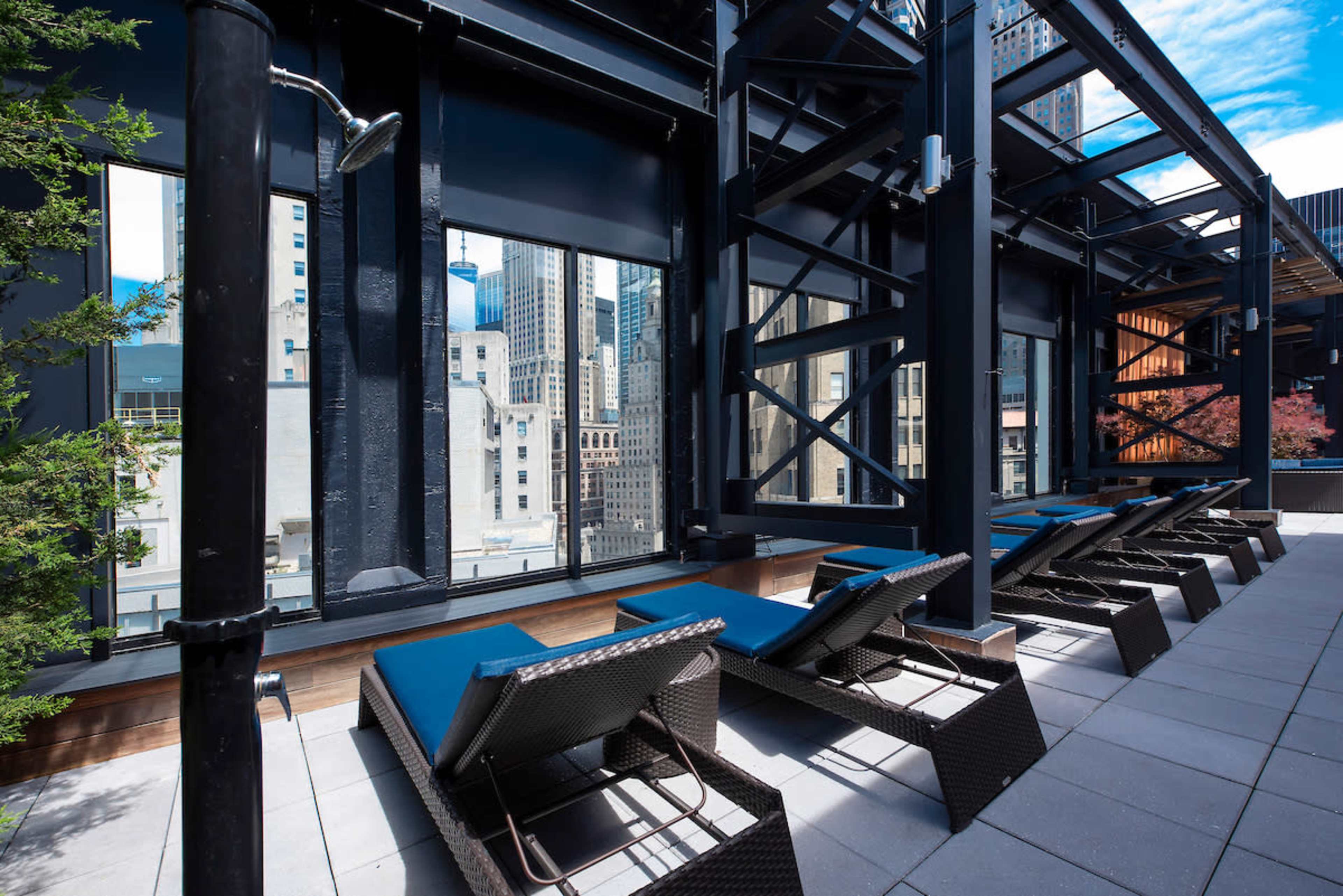A rooftop terrace features lined lounge chairs with large windows showcasing city views.