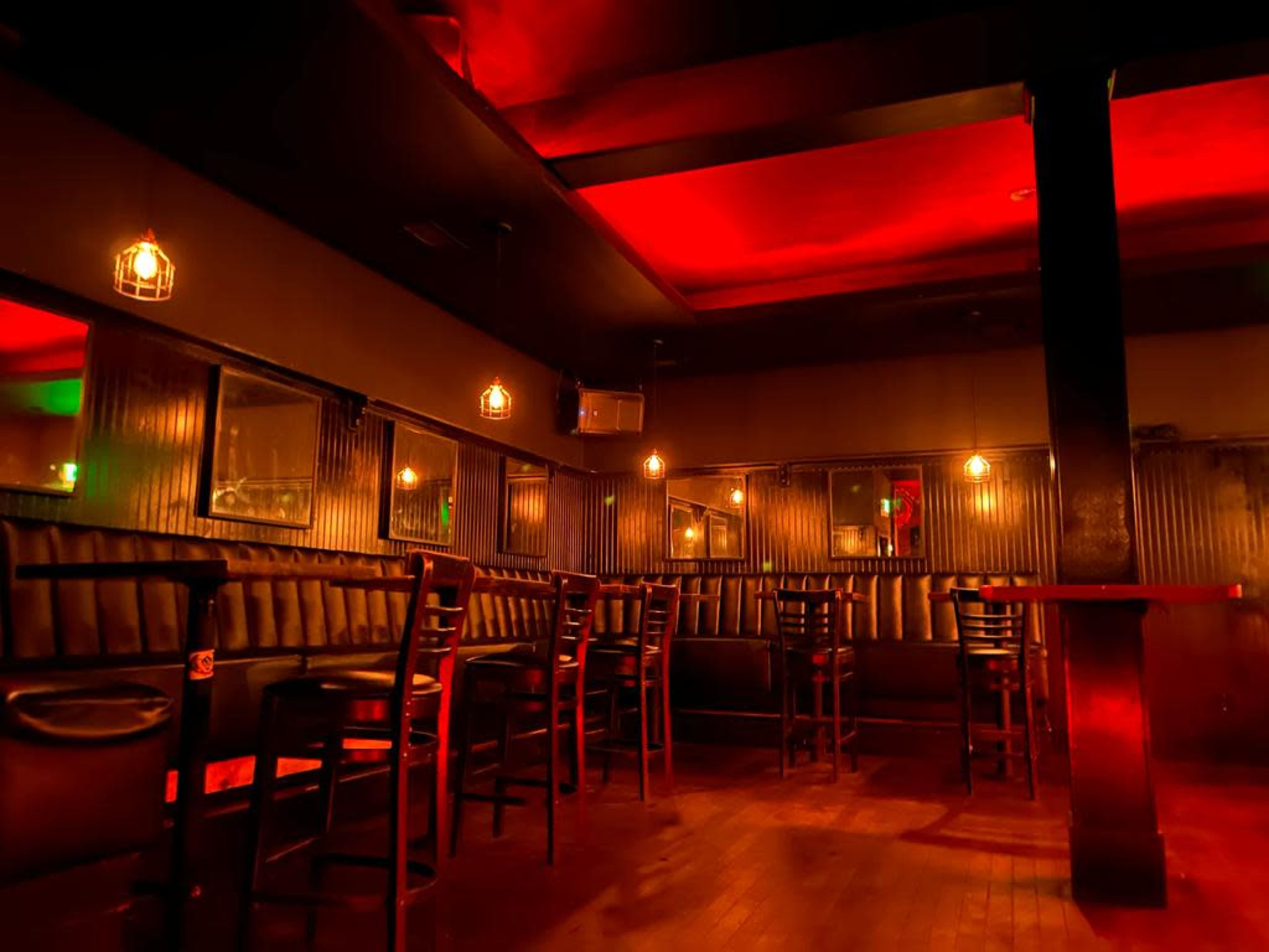 The image shows a dimly lit bar with empty wooden chairs and tables, illuminated by red and green lights.