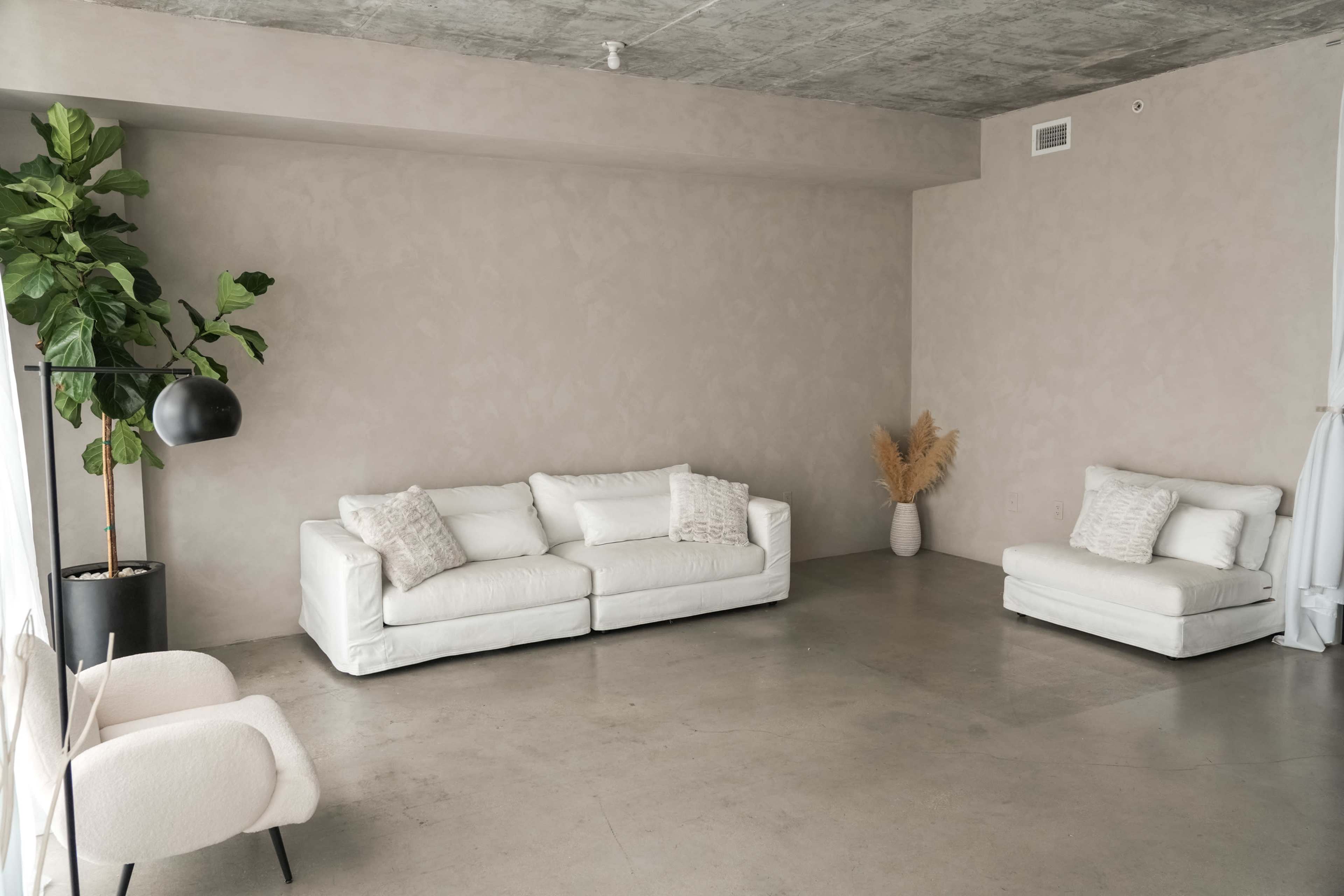 A minimalist living space featuring two white sofas, a potted plant, and a beige decorative vase.