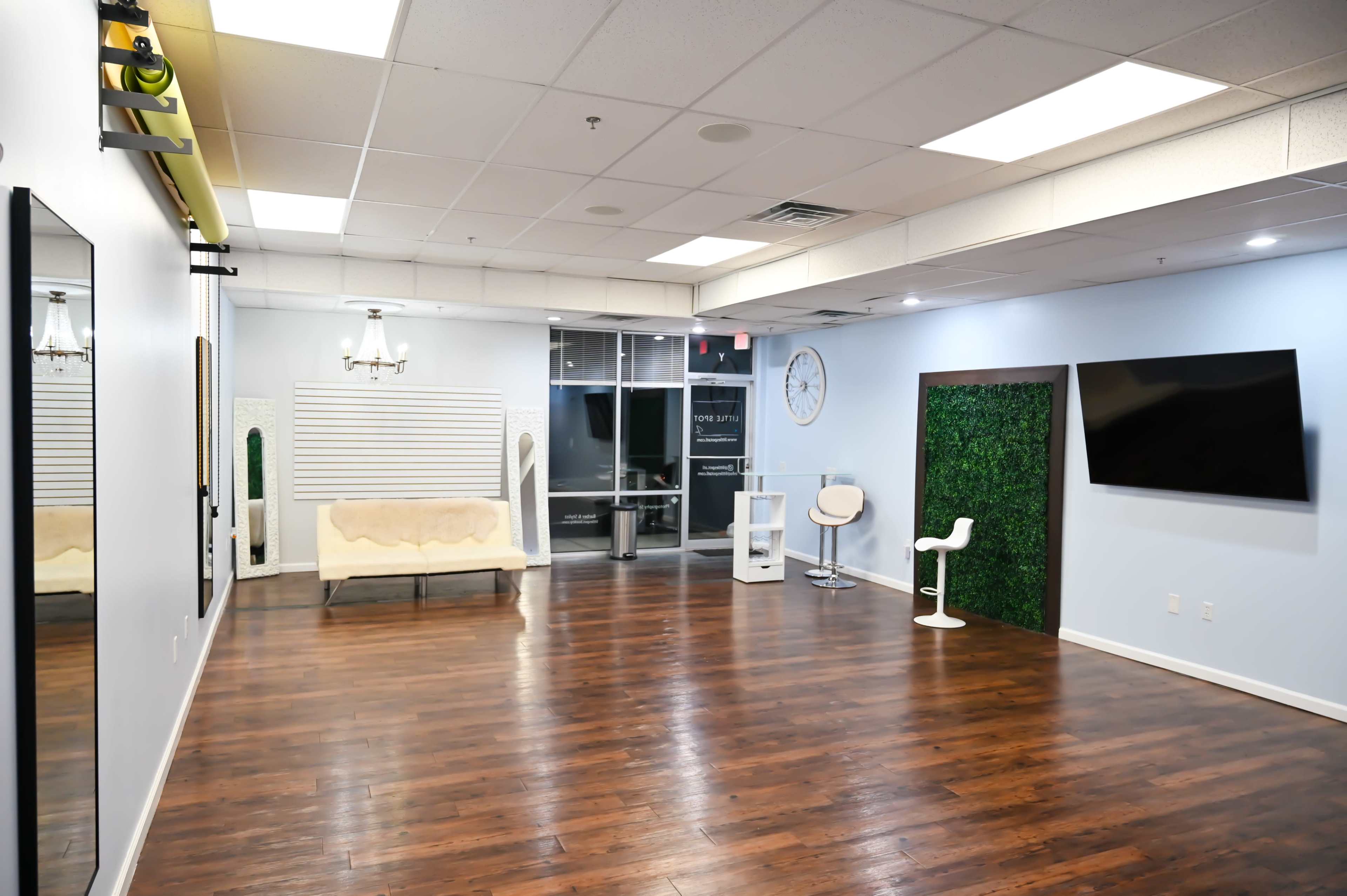 A spacious, well-lit room with hardwood flooring, featuring a seating area, a large mirror, and a decorative green wall.