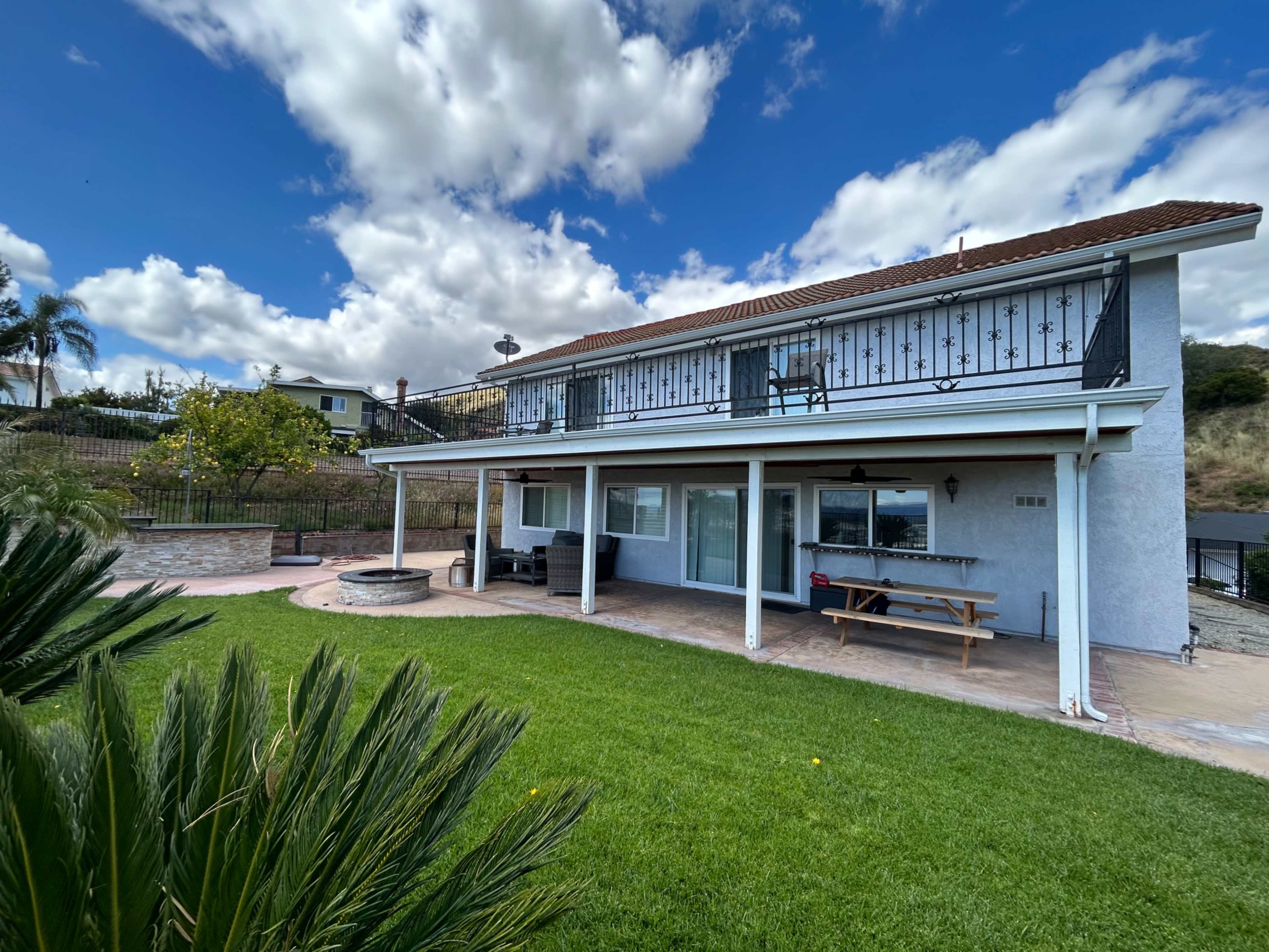 A two-story house with a spacious green yard, surrounded by various plants and under a partly cloudy sky.