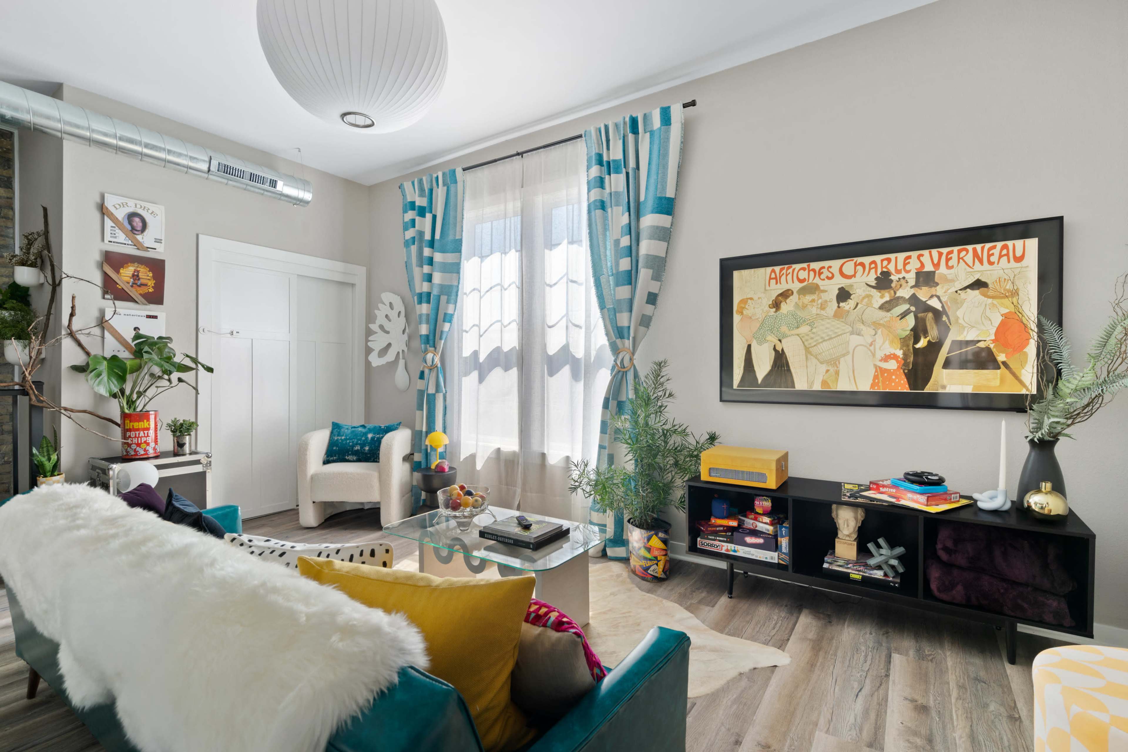 A cozy living room features a mix of modern furniture, colorful decor, and a vintage poster on the wall.