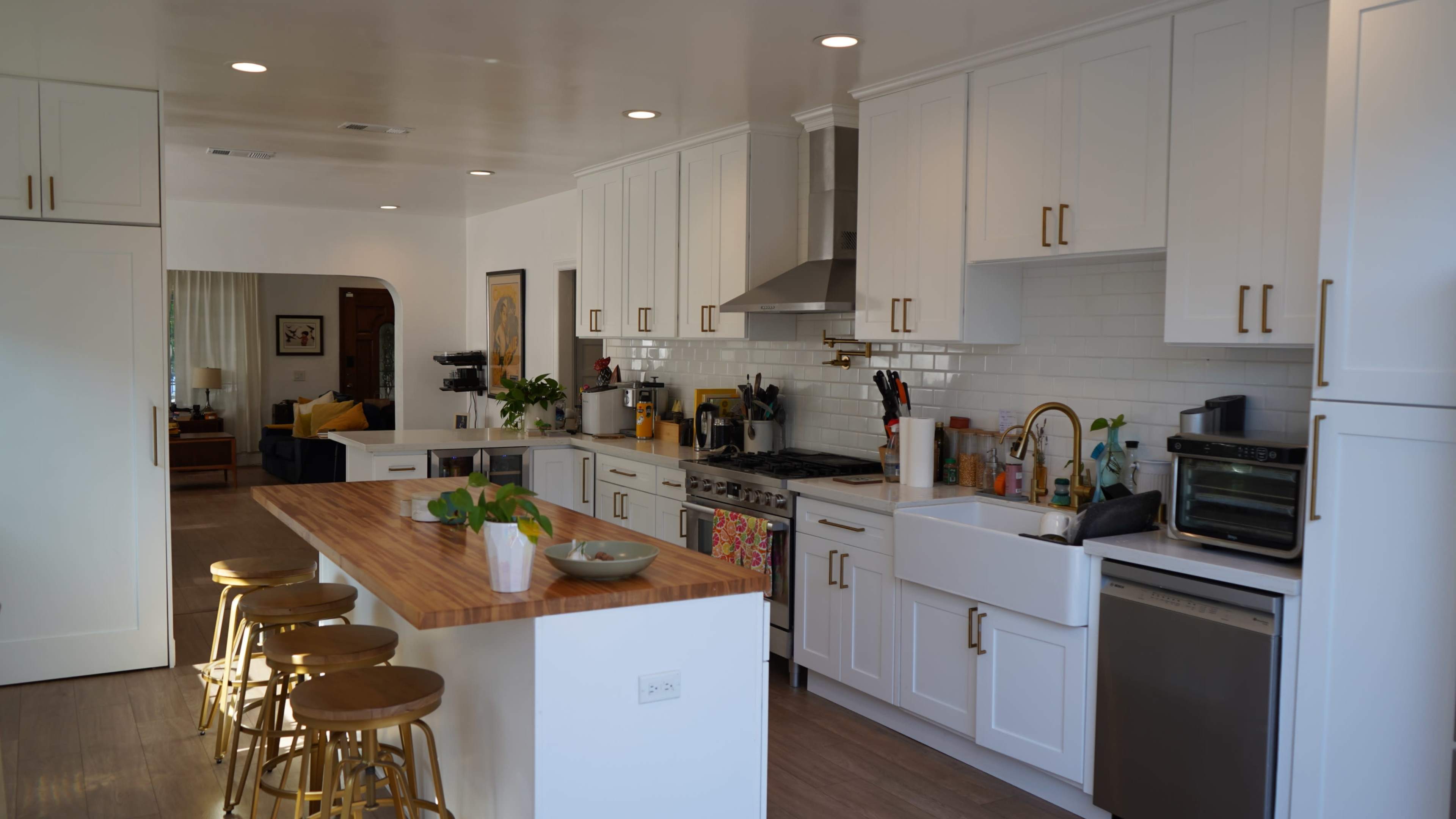 The image shows a modern kitchen with white cabinets, a large island with wooden countertops, and stainless steel appliances.