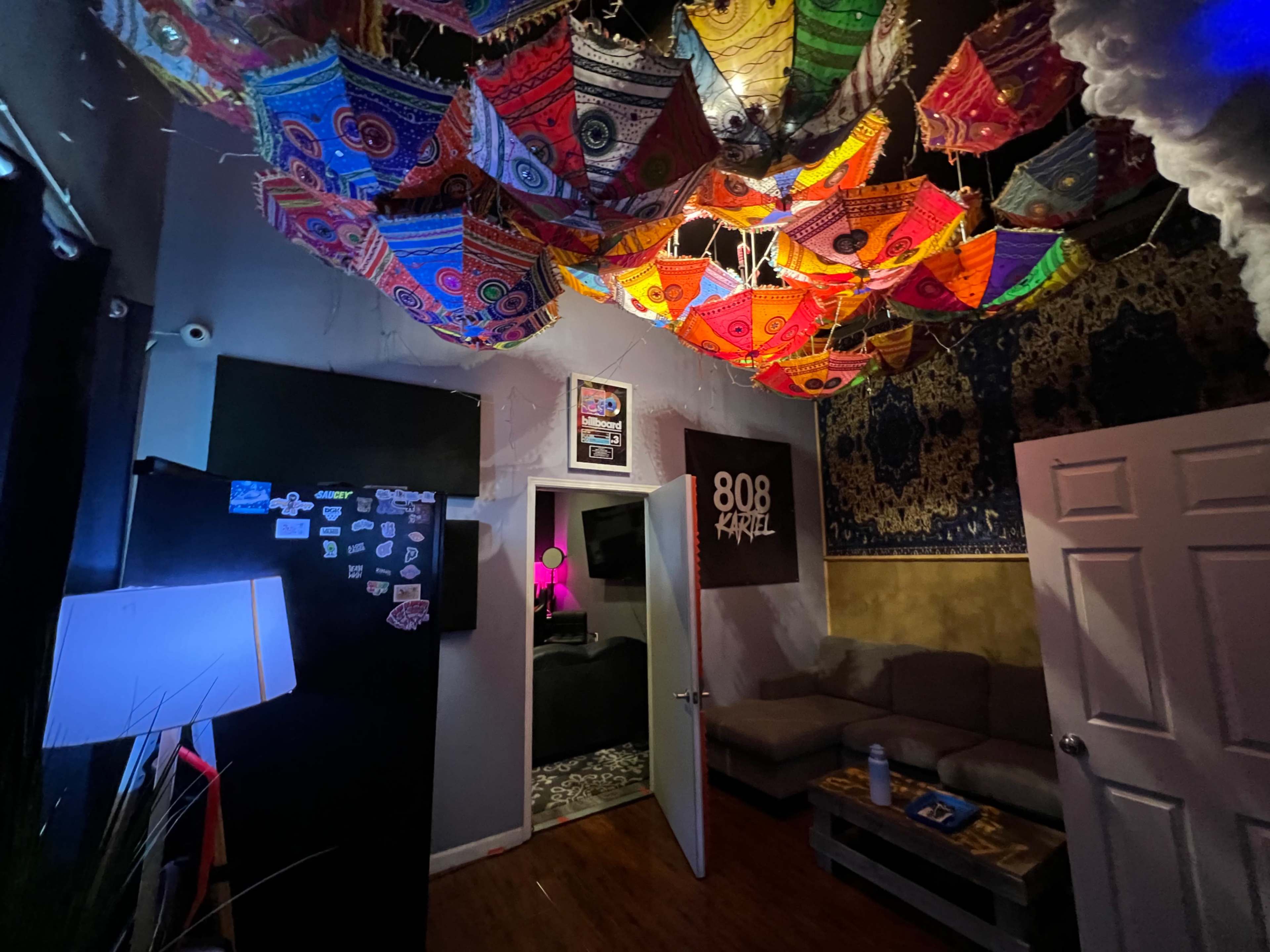The room features colorful umbrellas hanging from the ceiling, with a couch, door, and various decorations on the walls.